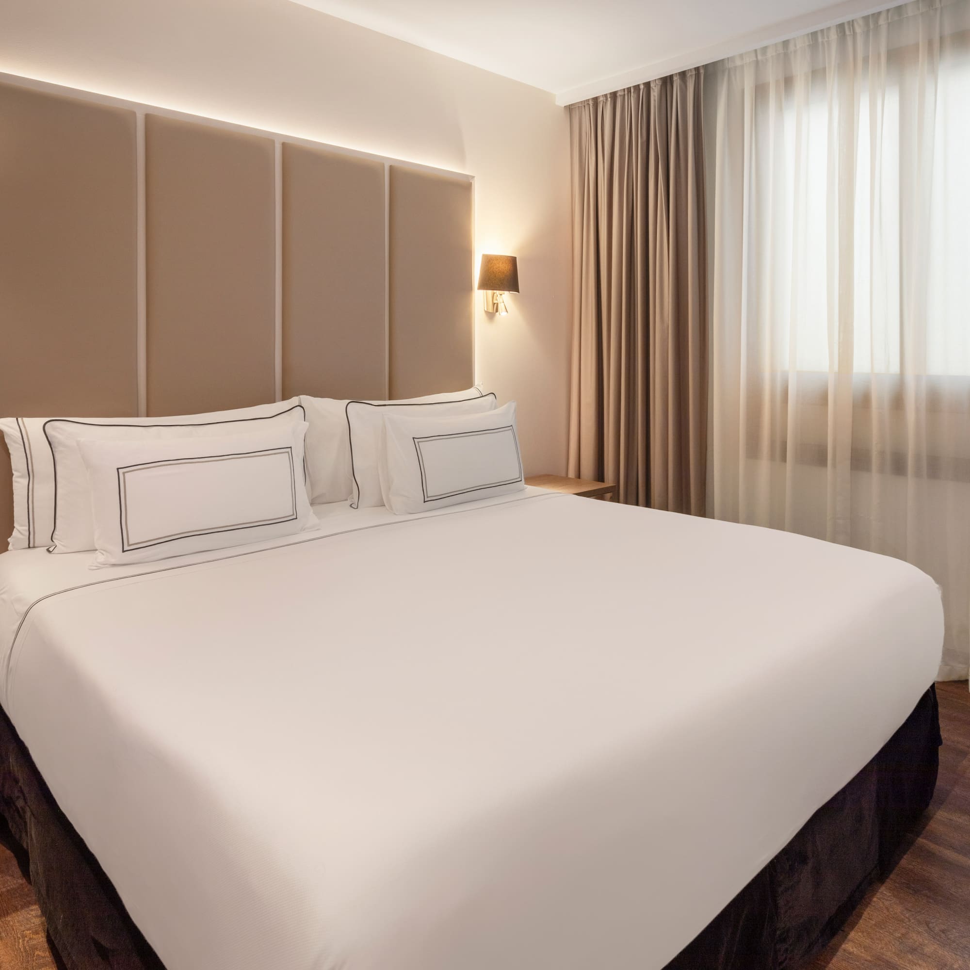 Modern hotel room with a large bed, beige headboard, and warm lighting.