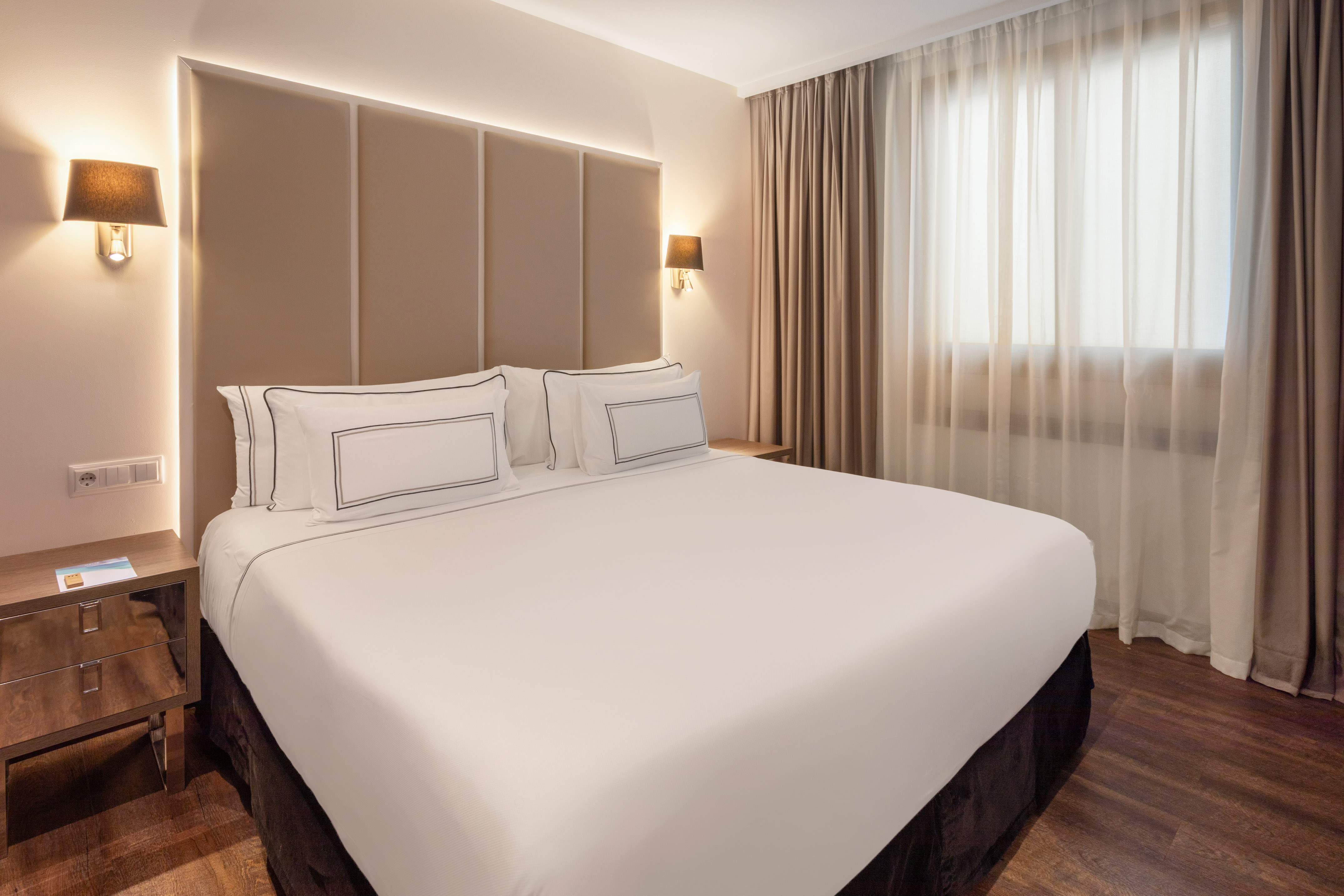 Modern hotel room with a large bed, beige headboard, and warm lighting.
