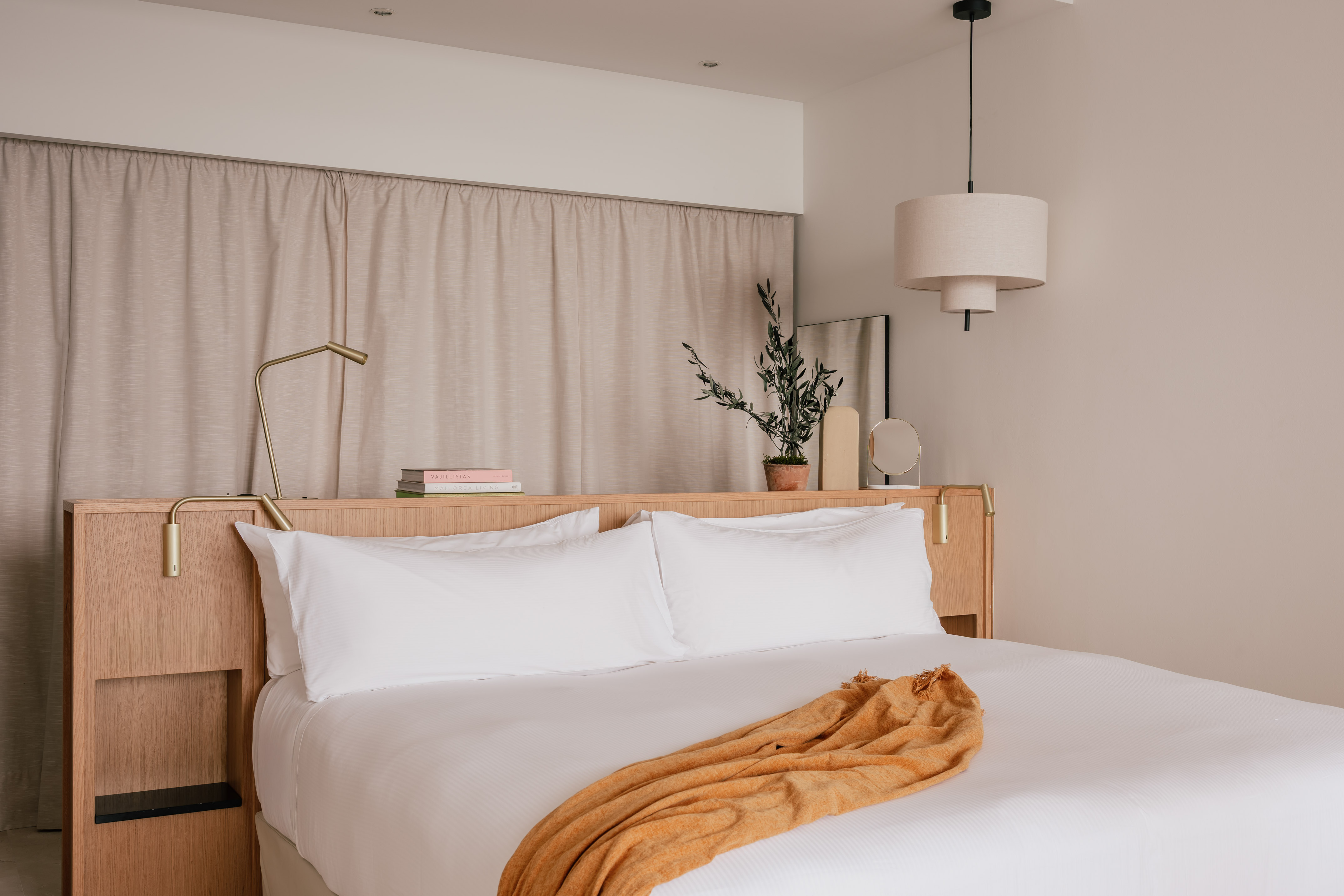 Modern hotel bedroom with wooden headboard, white bed, and orange accent throw.