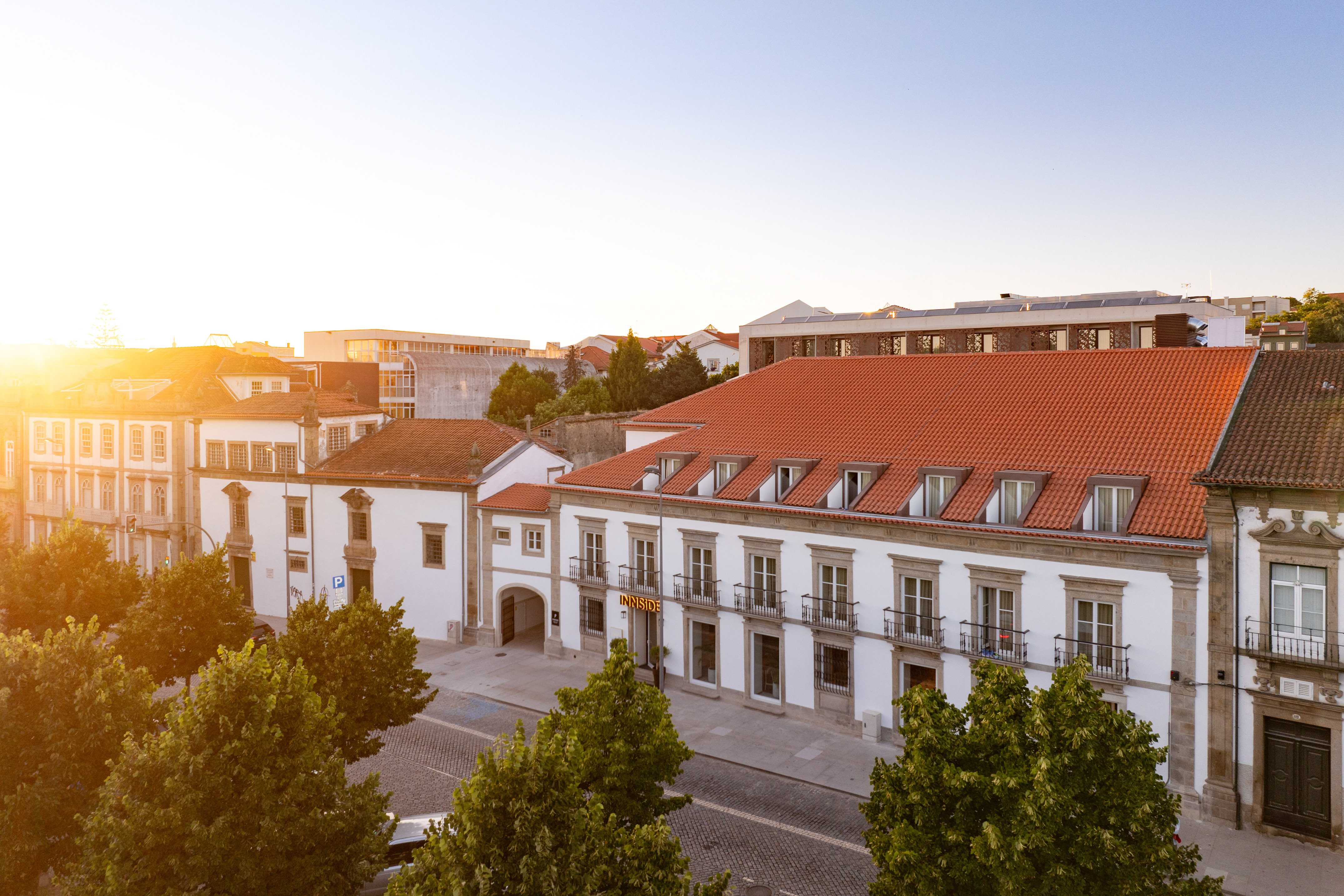 INNSiDE hotel building with red tiled roofs, white facade, and trees at sunrise.
