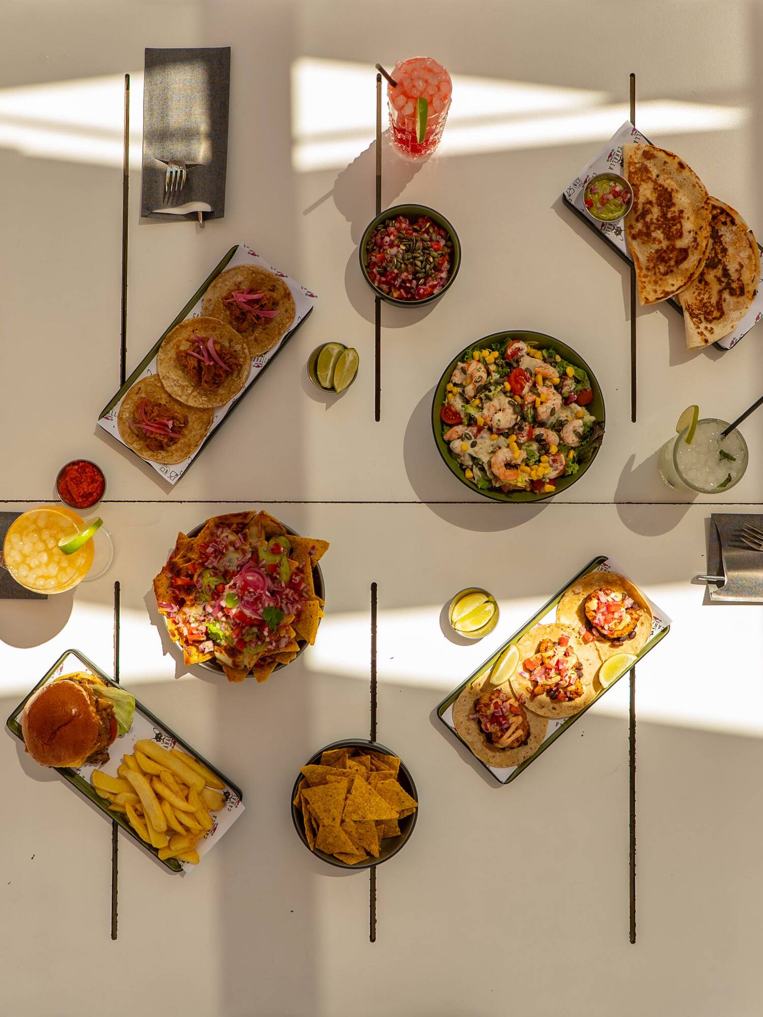 Mexican food feast: tacos, nachos, quesadillas, salad, burger, cocktails.