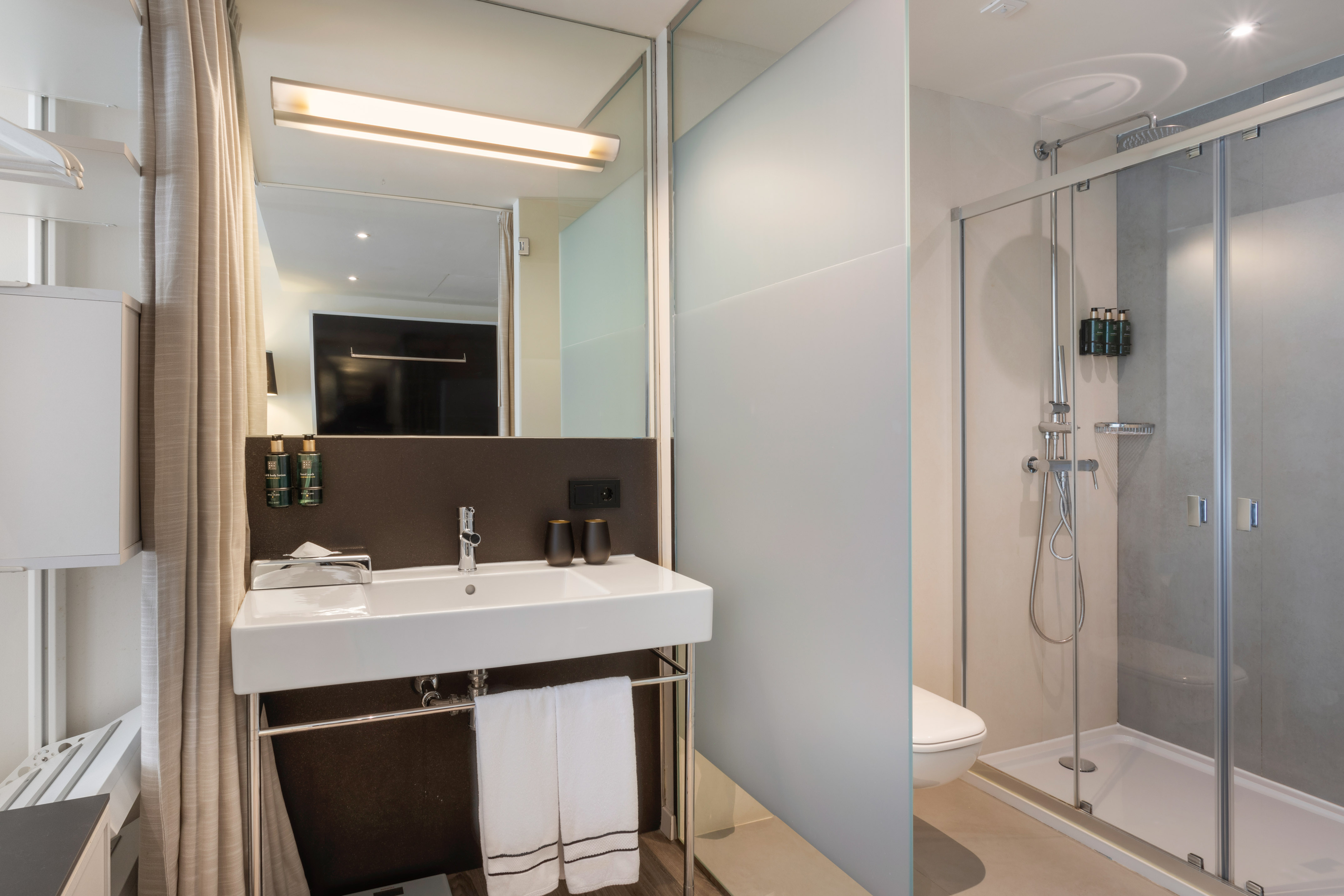 Modern hotel bathroom with sink, mirror, frosted glass shower, and toilet.