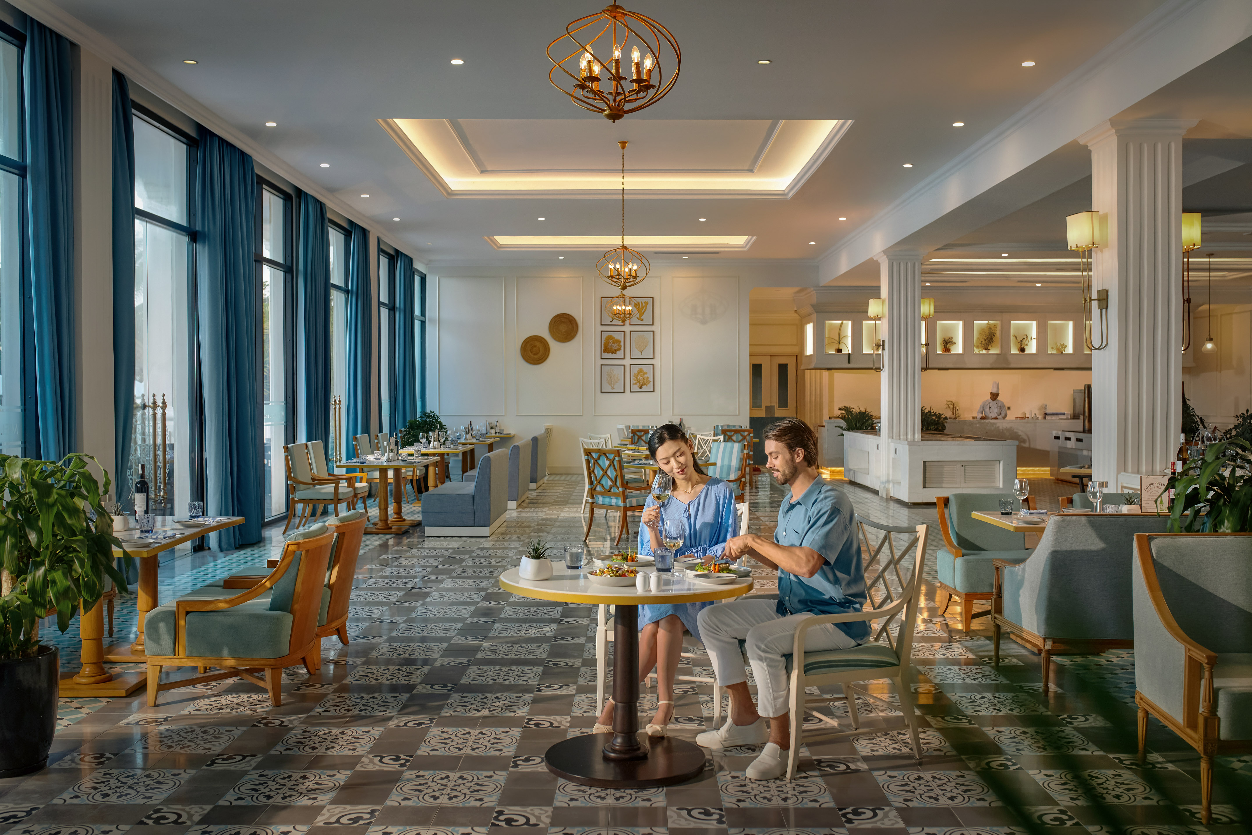 Couple dining in elegant restaurant with blue curtains and chandeliers.