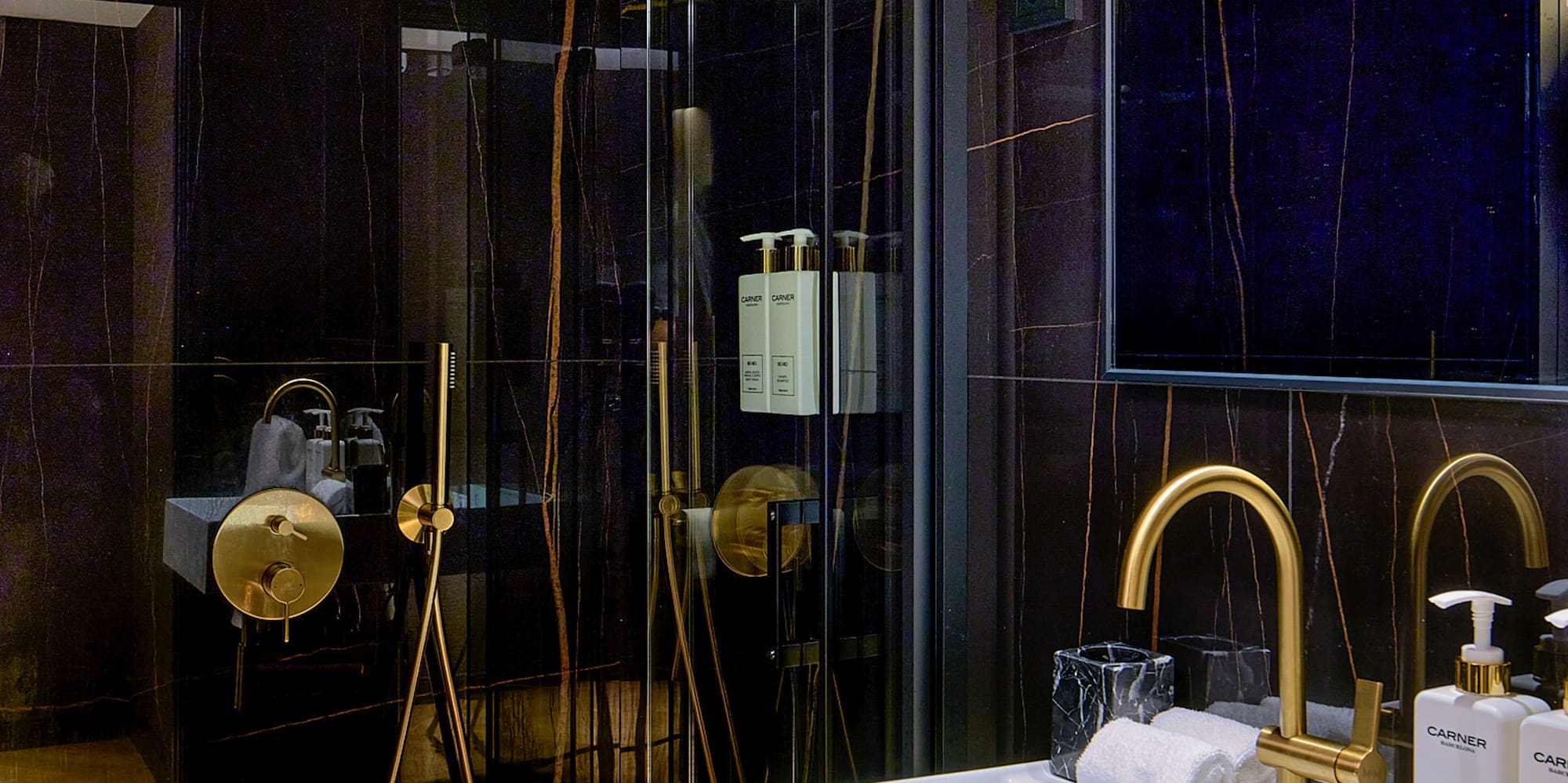 Luxury bathroom with black marble walls, gold fixtures, white sink, and glass shower.