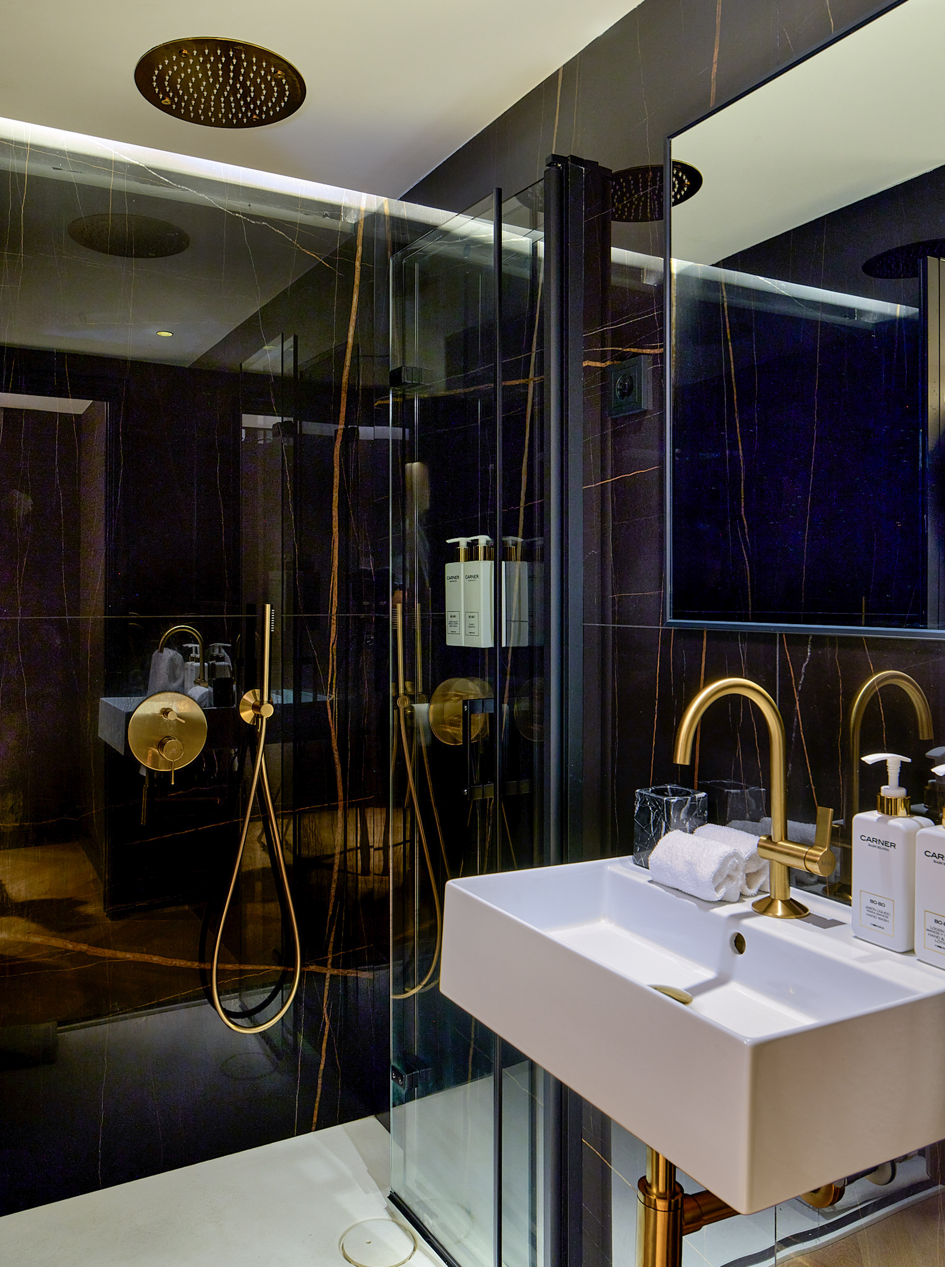 Luxury bathroom with black marble walls, gold fixtures, white sink, and glass shower.