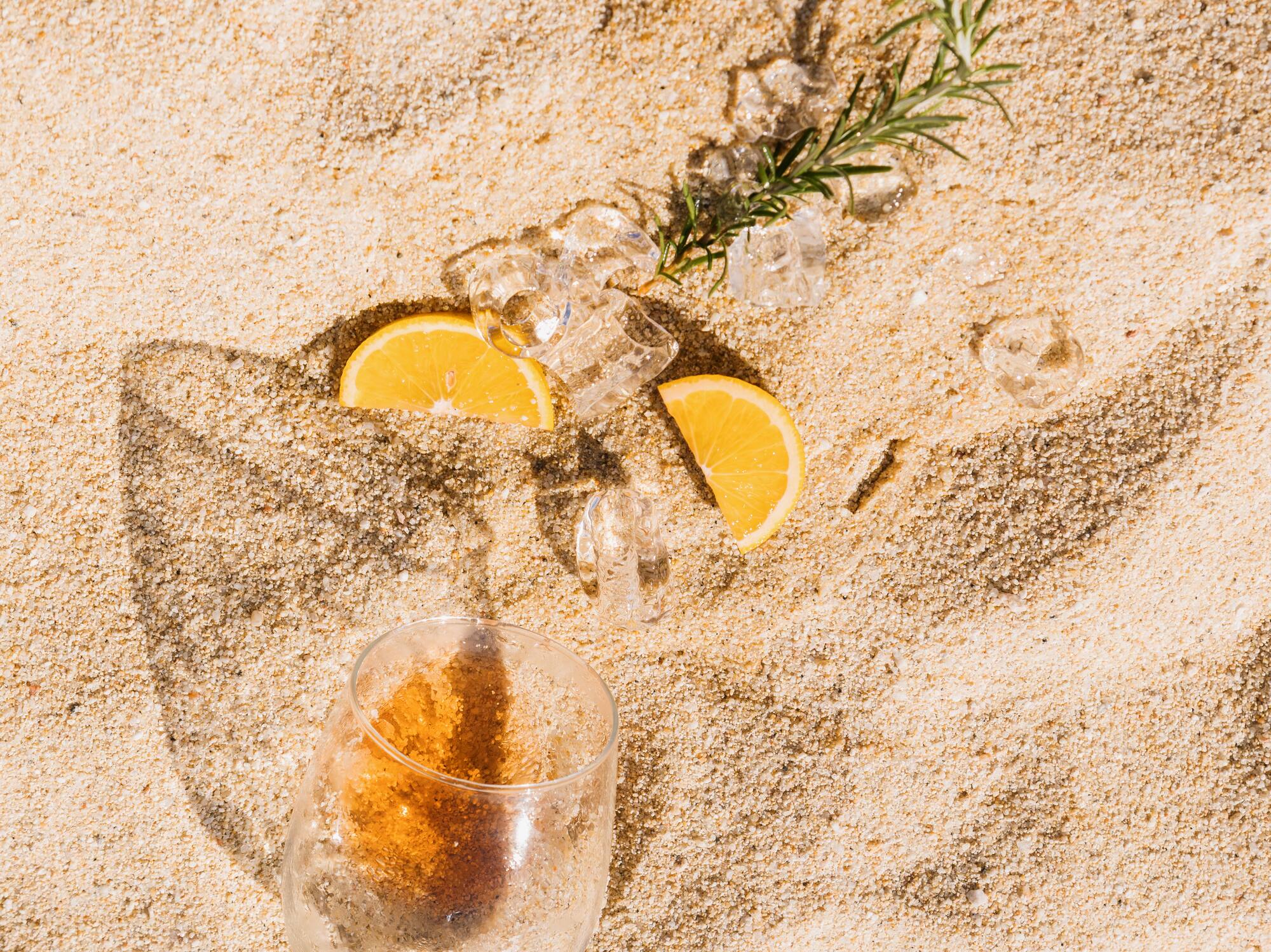 a glass of wine and ice cubes on sand
