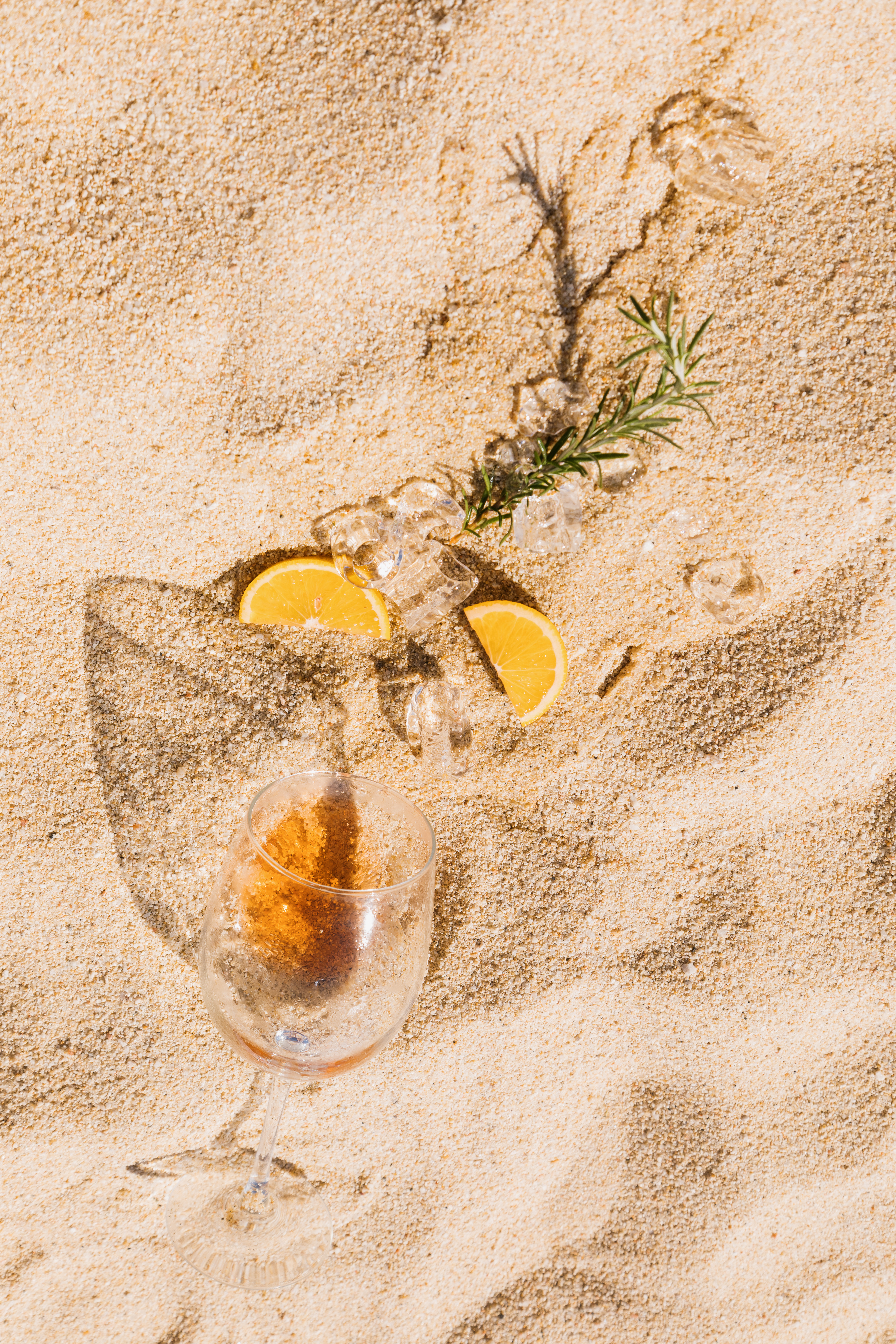 a glass of wine and ice cubes on sand