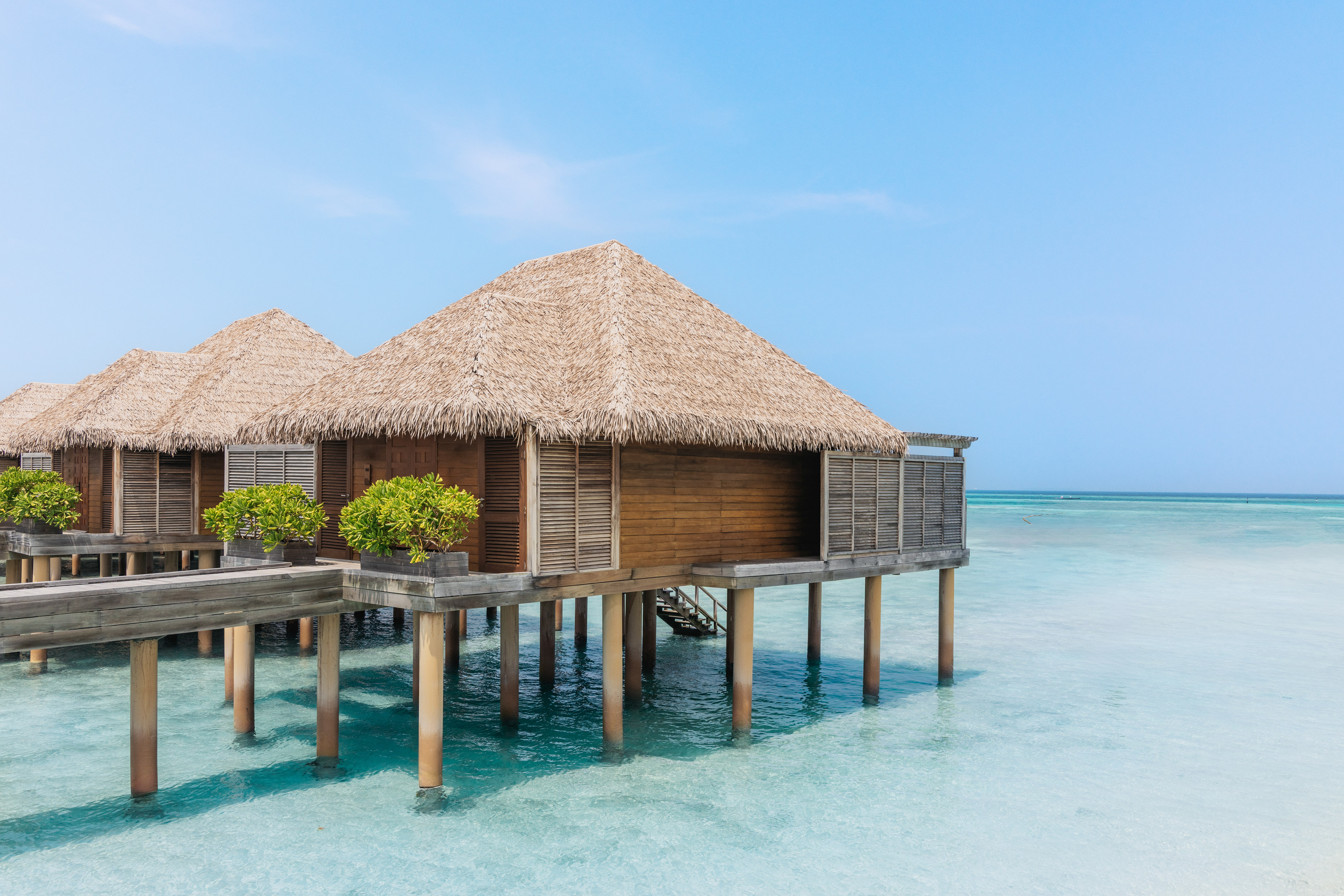 Thatched roof overwater bungalows above clear turquoise ocean water, tropical resort.