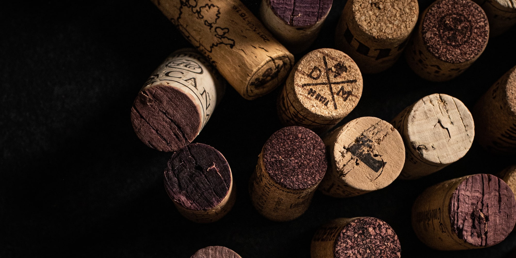 Scattered wine corks with red wine marks and winery stamps on black.