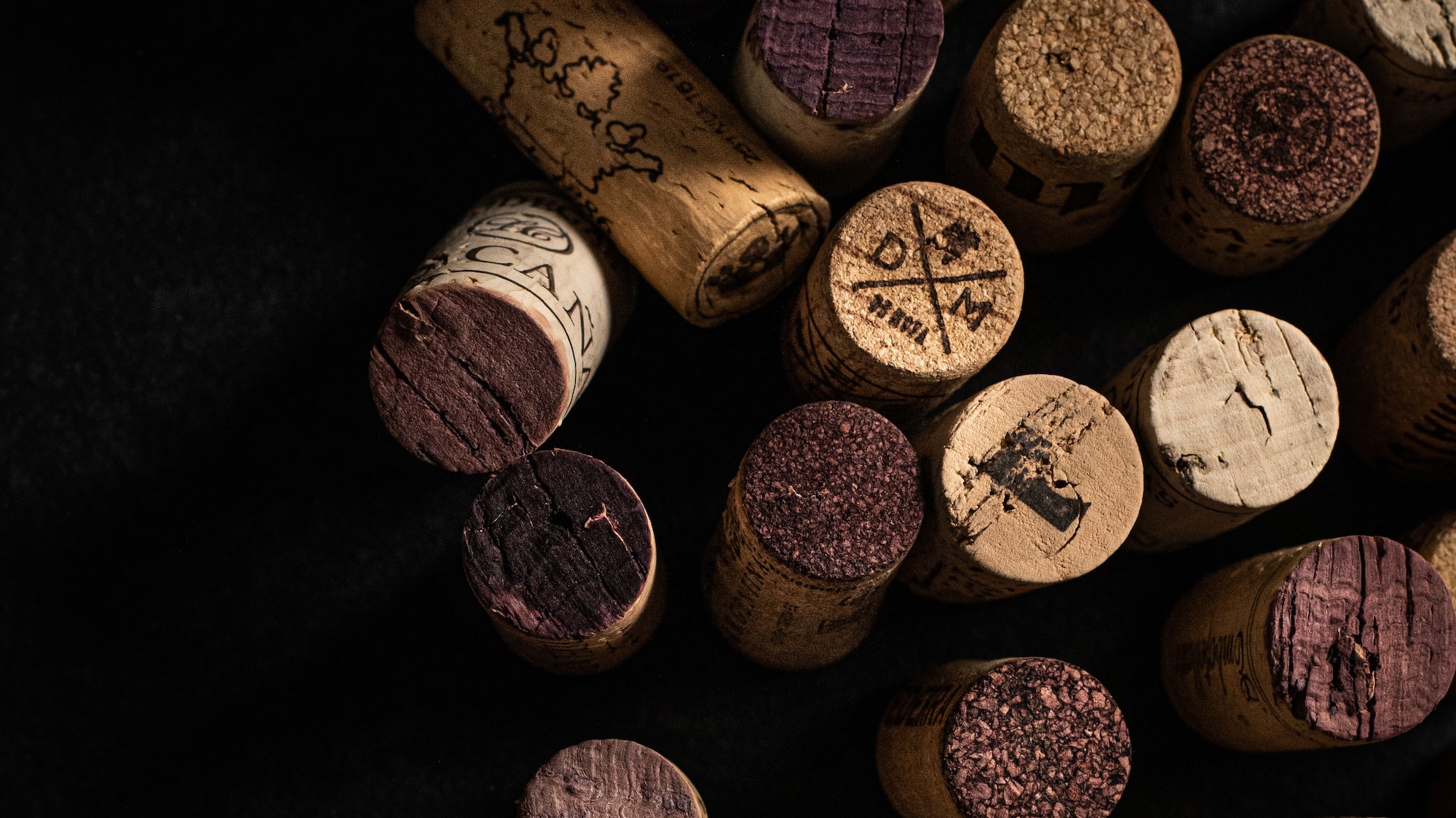 Scattered wine corks with red wine marks and winery stamps on black.