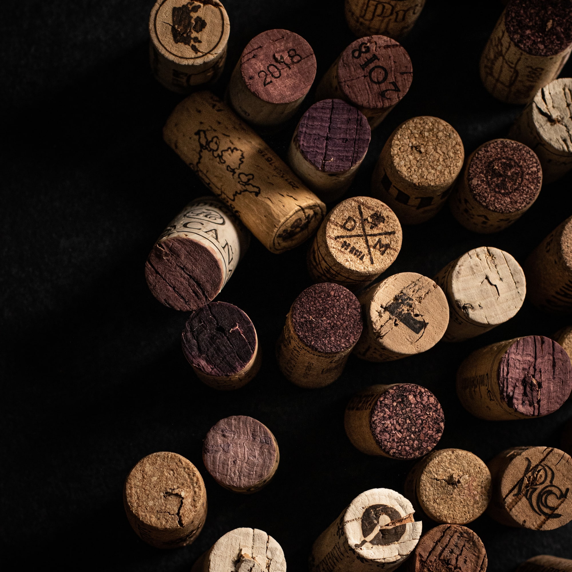 Scattered wine corks with red wine marks and winery stamps on black.