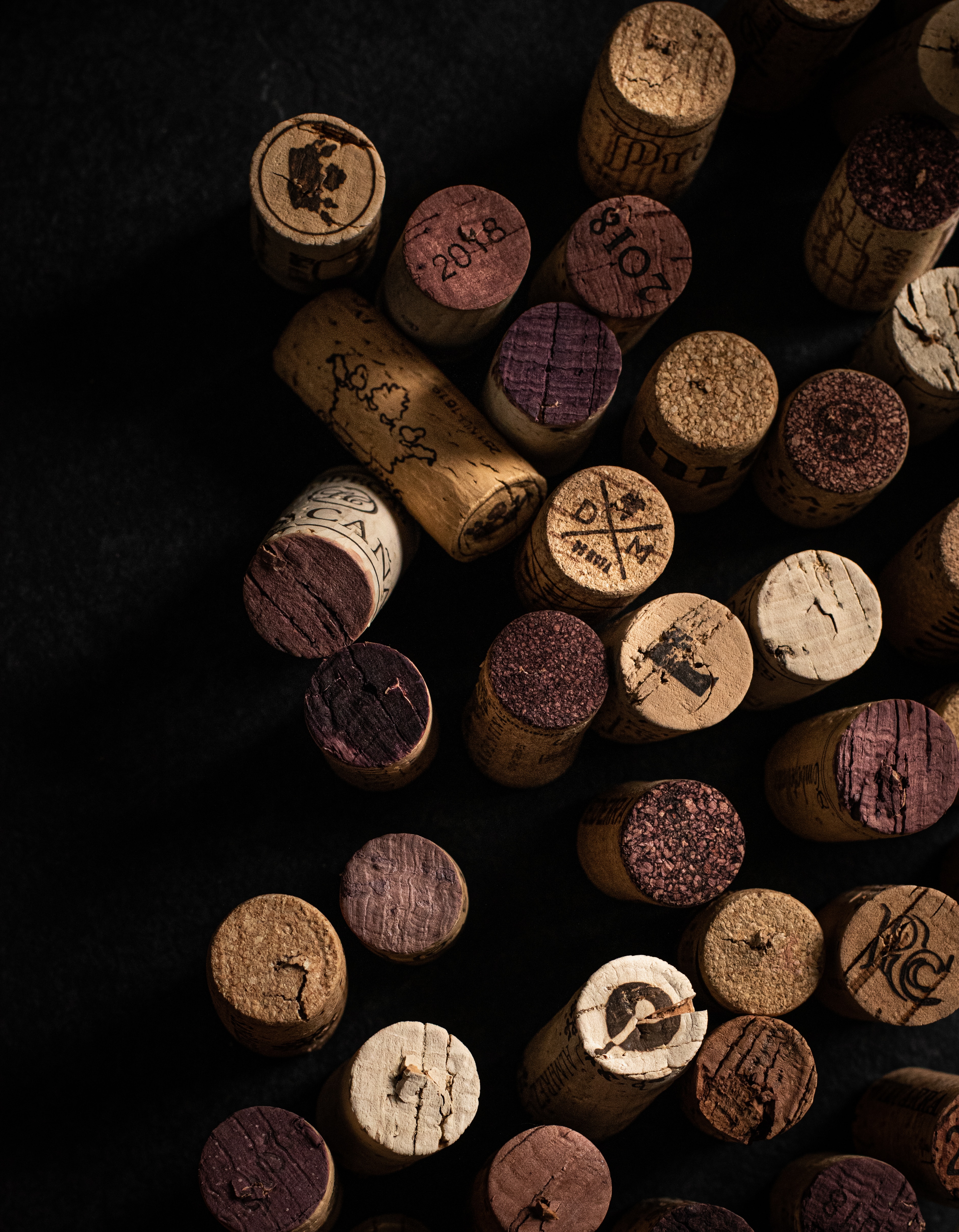 Scattered wine corks with red wine marks and winery stamps on black.