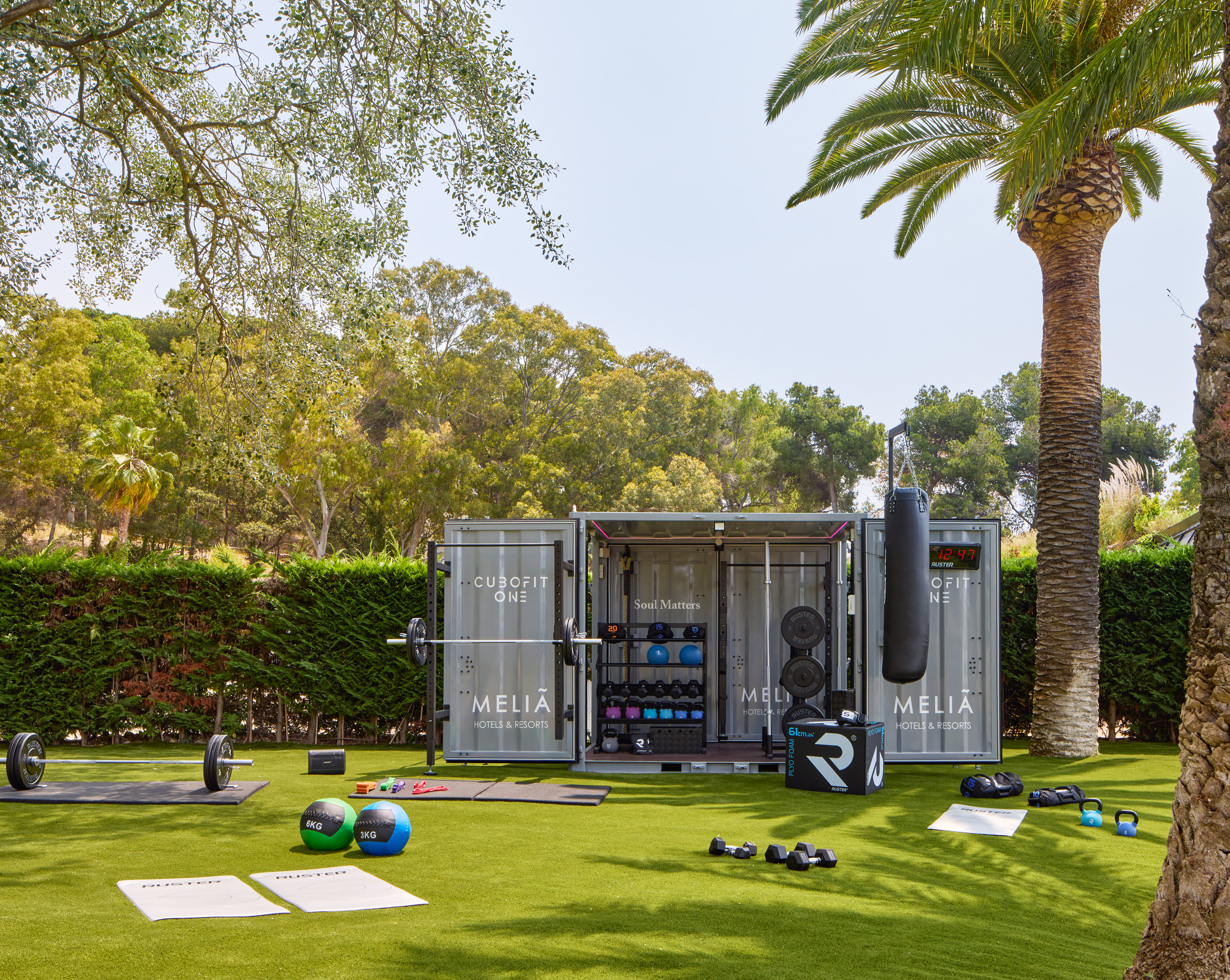 Melia Cubofit outdoor gym container with diverse fitness equipment on green grass.