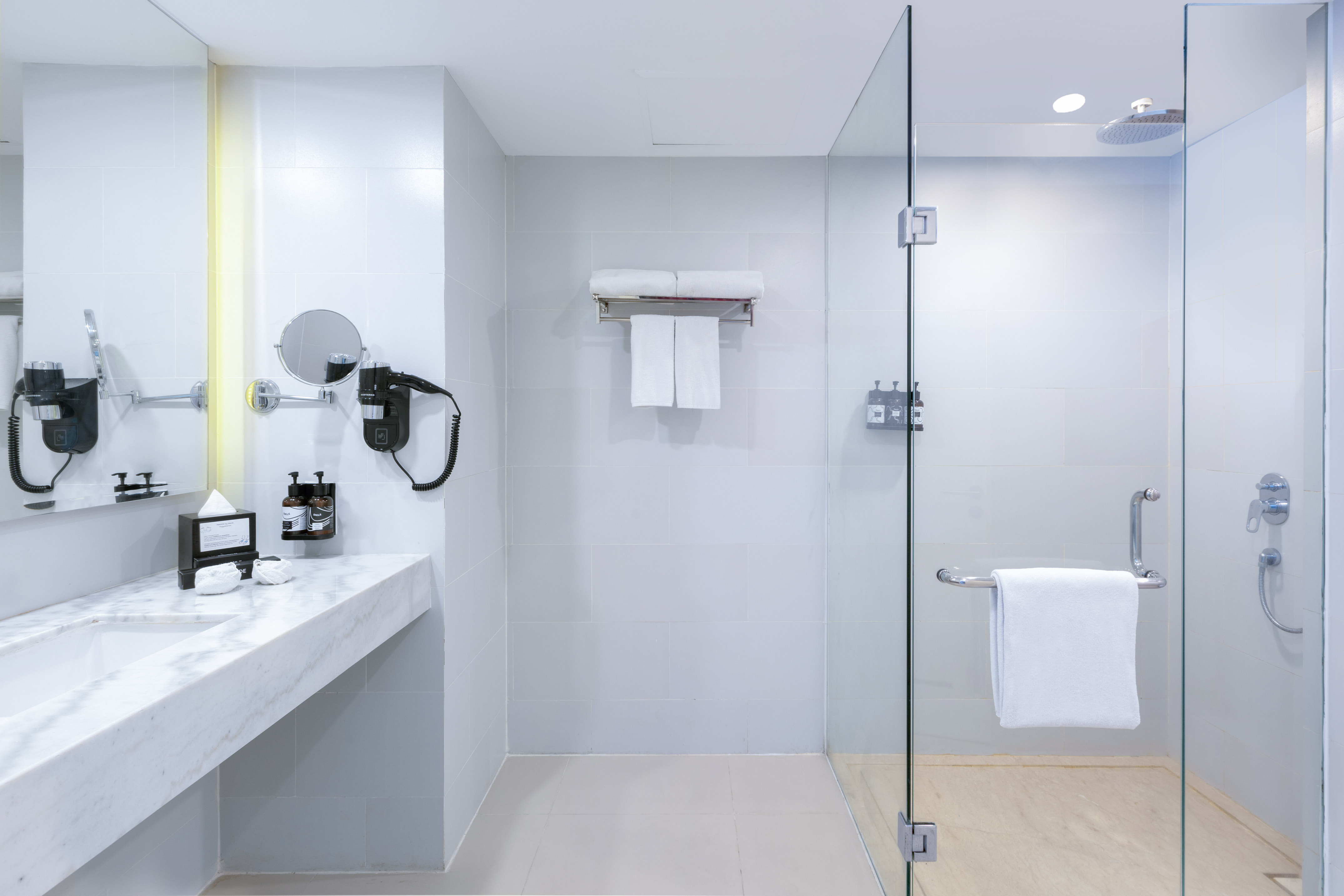 Modern hotel bathroom with marble vanity, glass walk-in shower, white towels.
