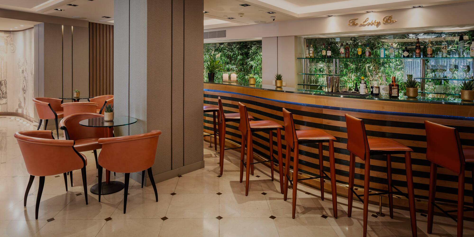 Modern hotel lobby bar with brown leather stools, lounge area, and green backdrop.