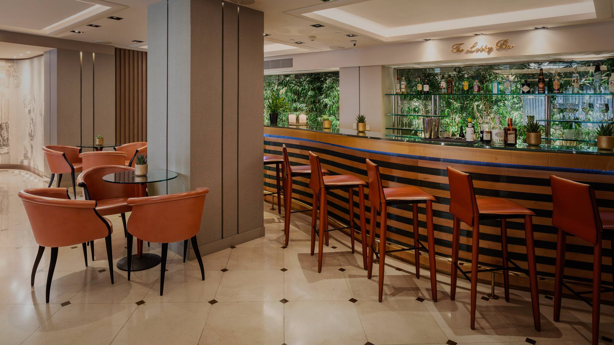 Modern hotel lobby bar with brown leather stools, lounge area, and green backdrop.