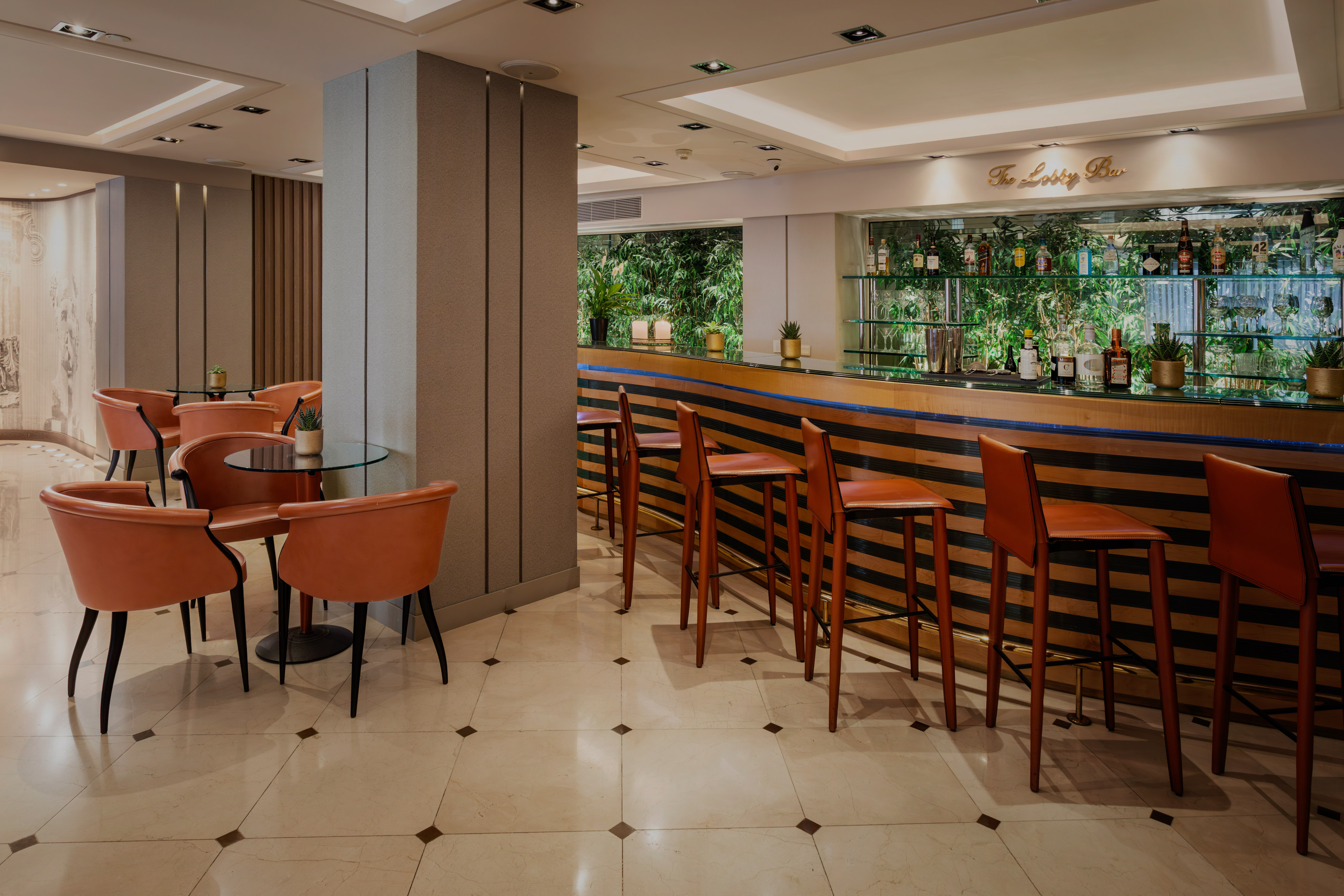 Modern hotel lobby bar with brown leather stools, lounge area, and green backdrop.