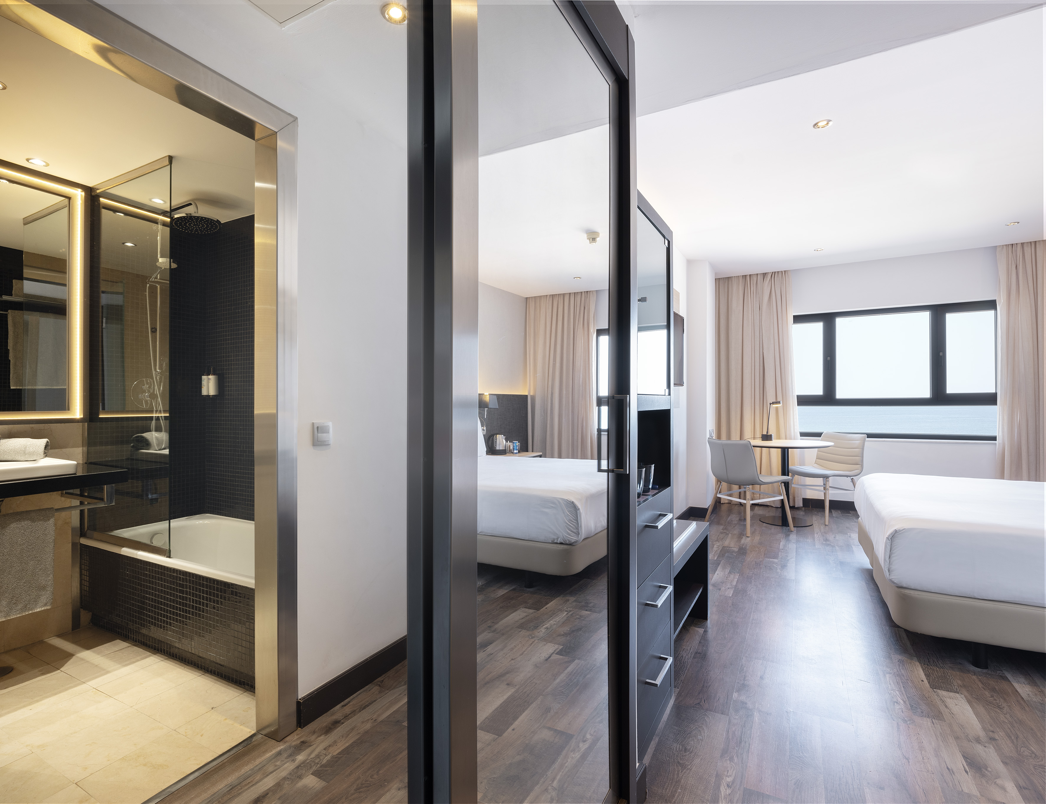 Spacious modern hotel room featuring two beds, full bathroom, and ocean view.