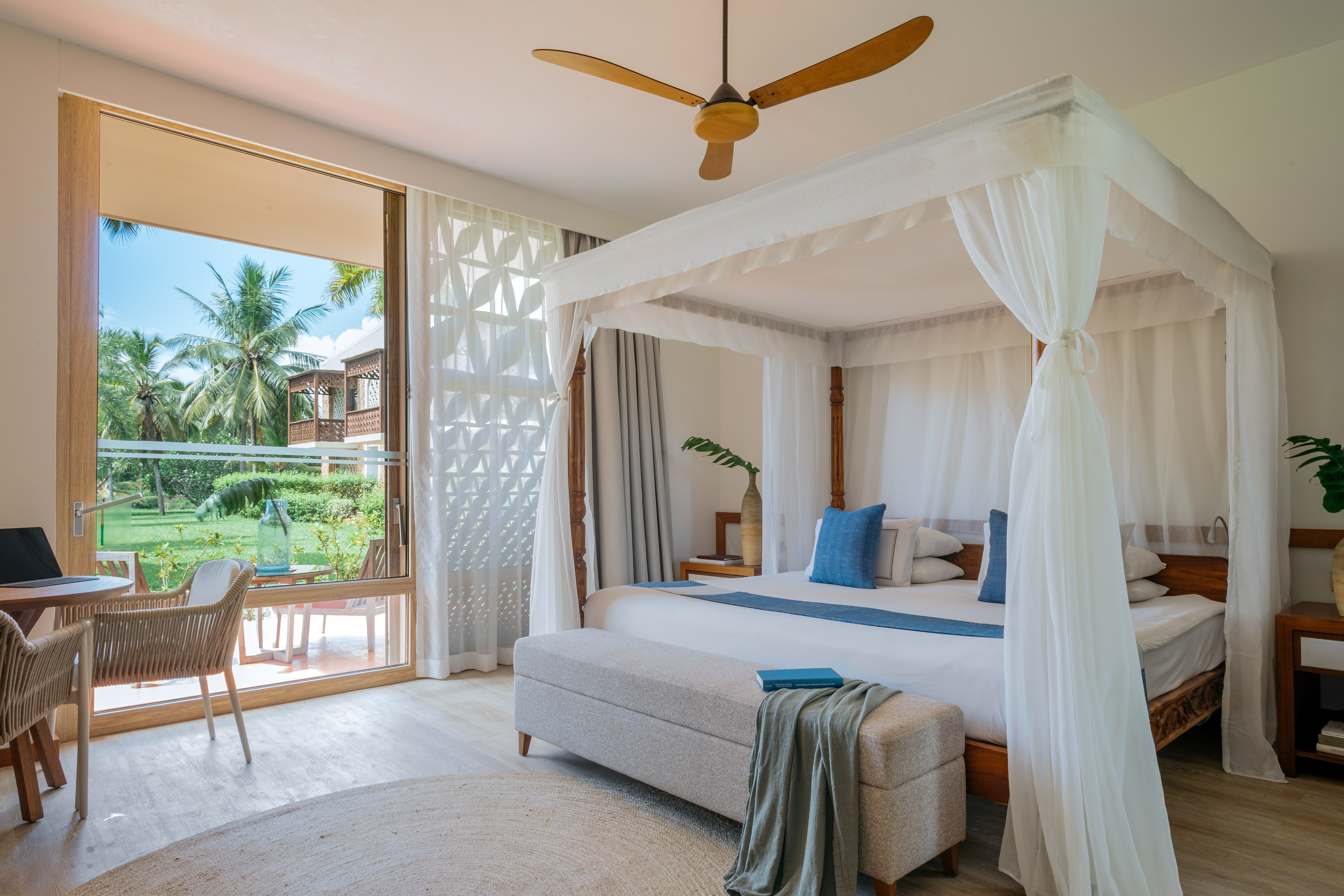 Tropical hotel bedroom with canopy bed, lush garden view, and ceiling fan.