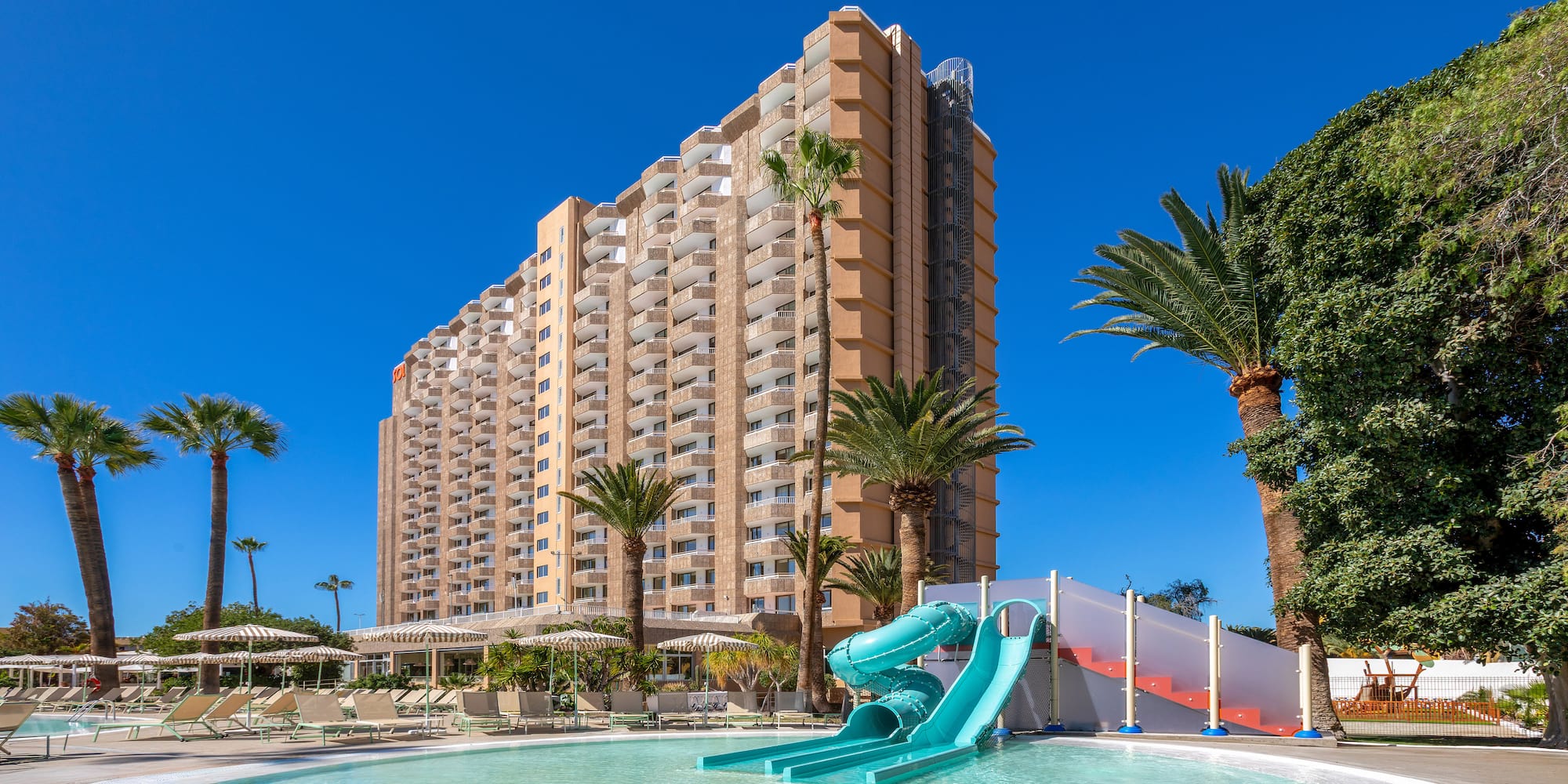 a pool with a slide and palm trees in front of a building