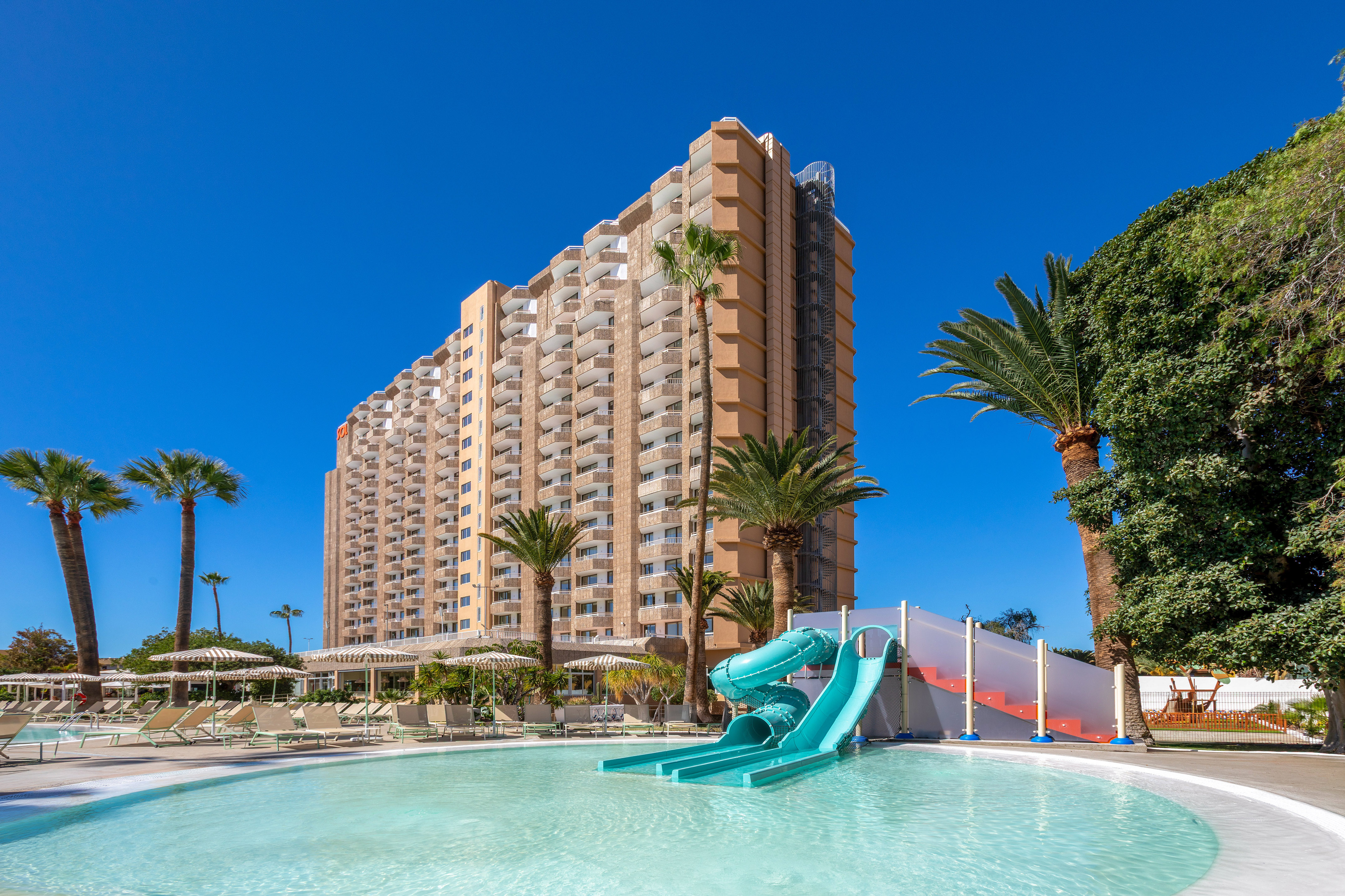 Tropical hotel resort with pool, blue water slide, and palm trees.