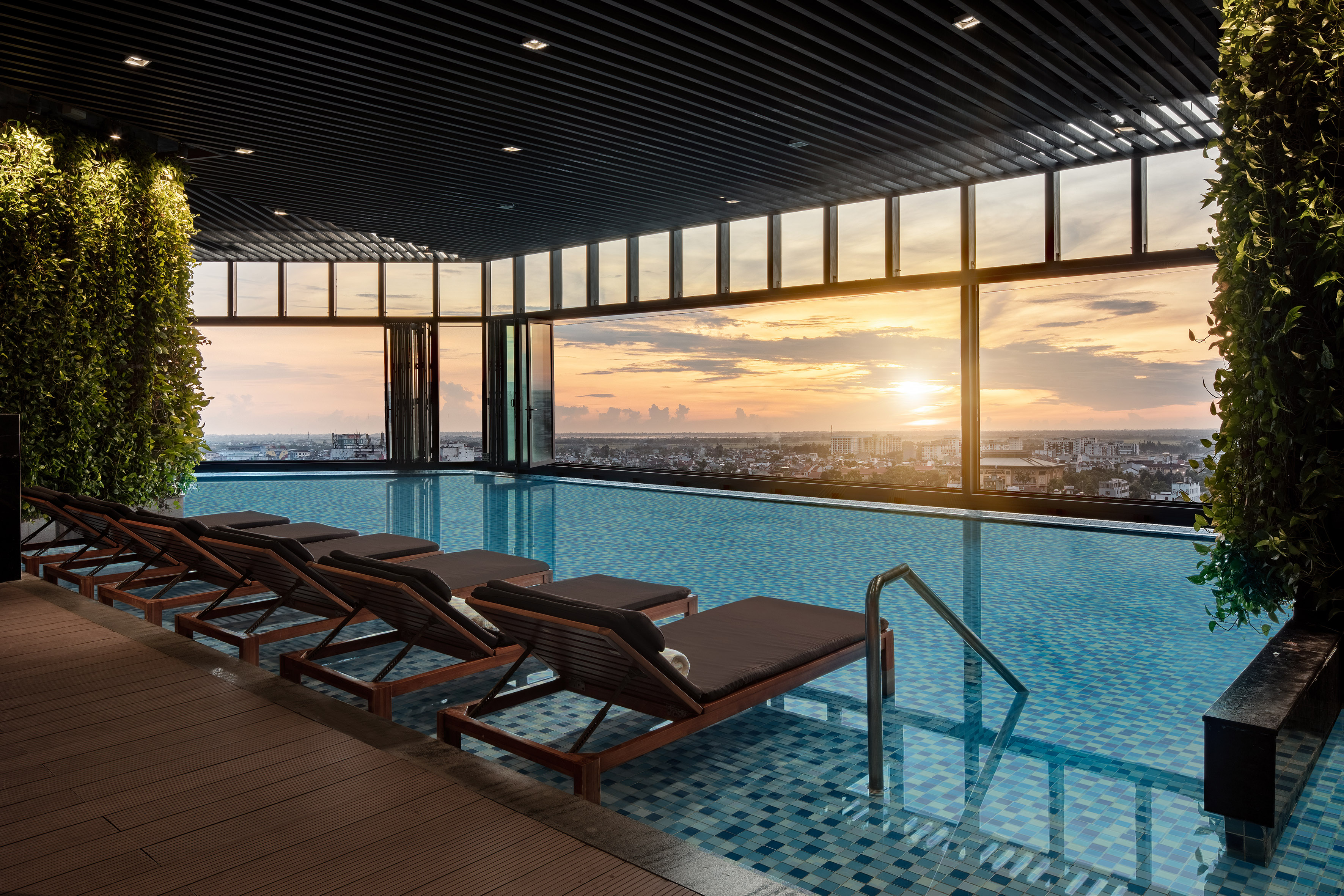 Modern rooftop pool with sunset city view and lounge chairs.