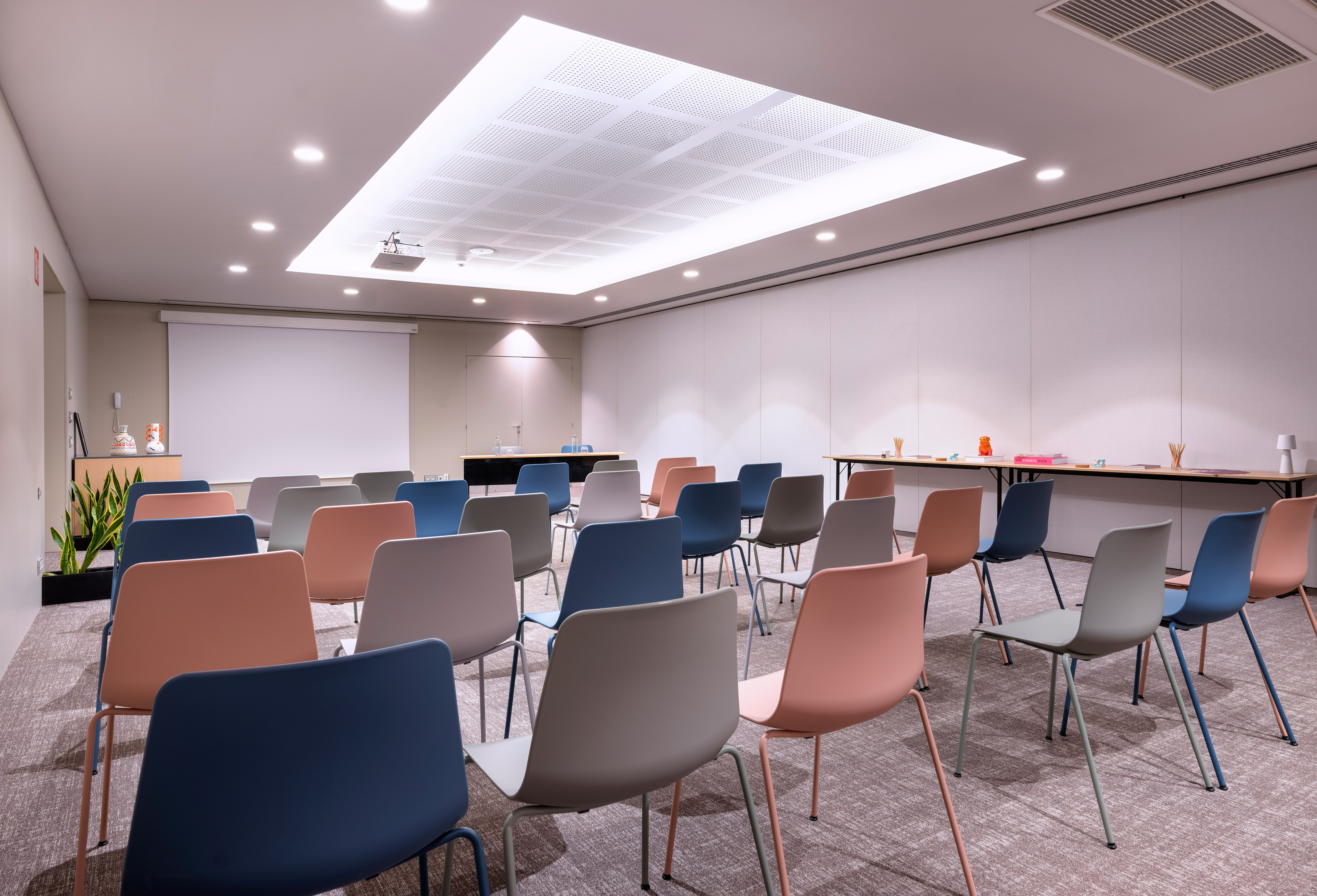 Modern meeting room with colorful chairs, projection screen, and bright lighting.