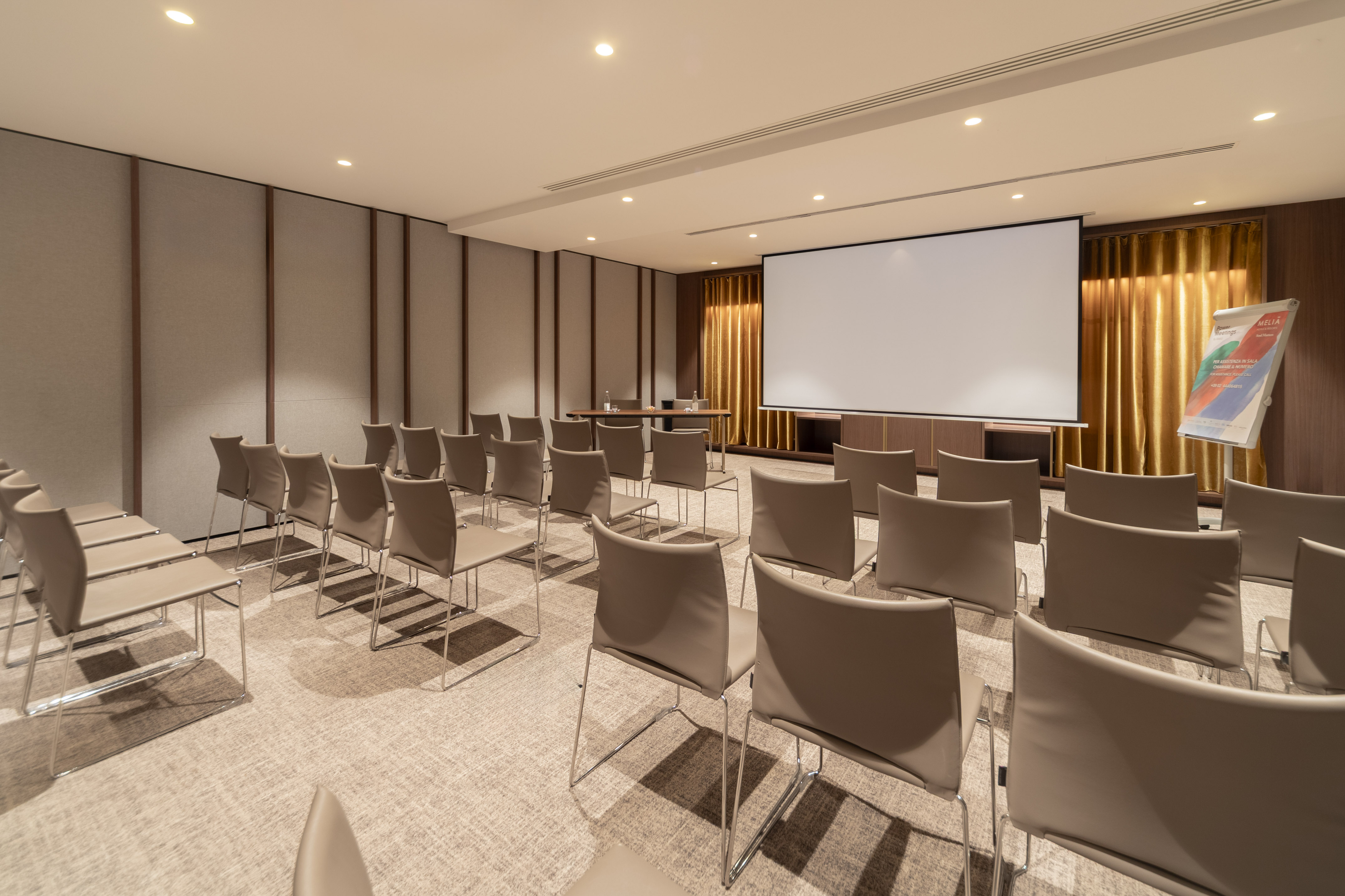 Modern meeting room with beige chairs, projector screen, and presentation area.