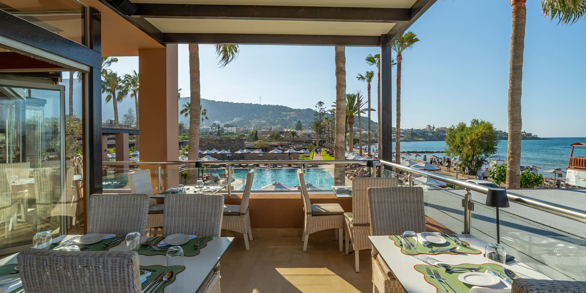Beachfront restaurant terrace with pool, sea views, and palm trees.