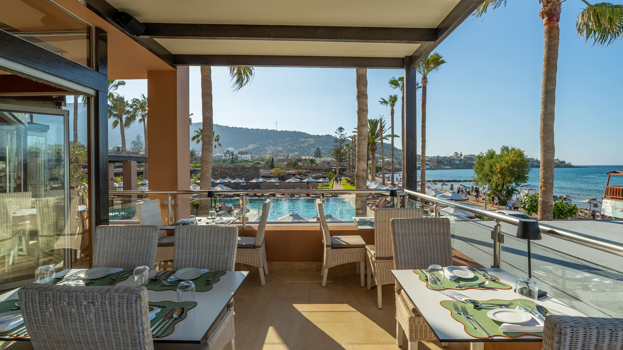 Beachfront restaurant terrace with pool, sea views, and palm trees.