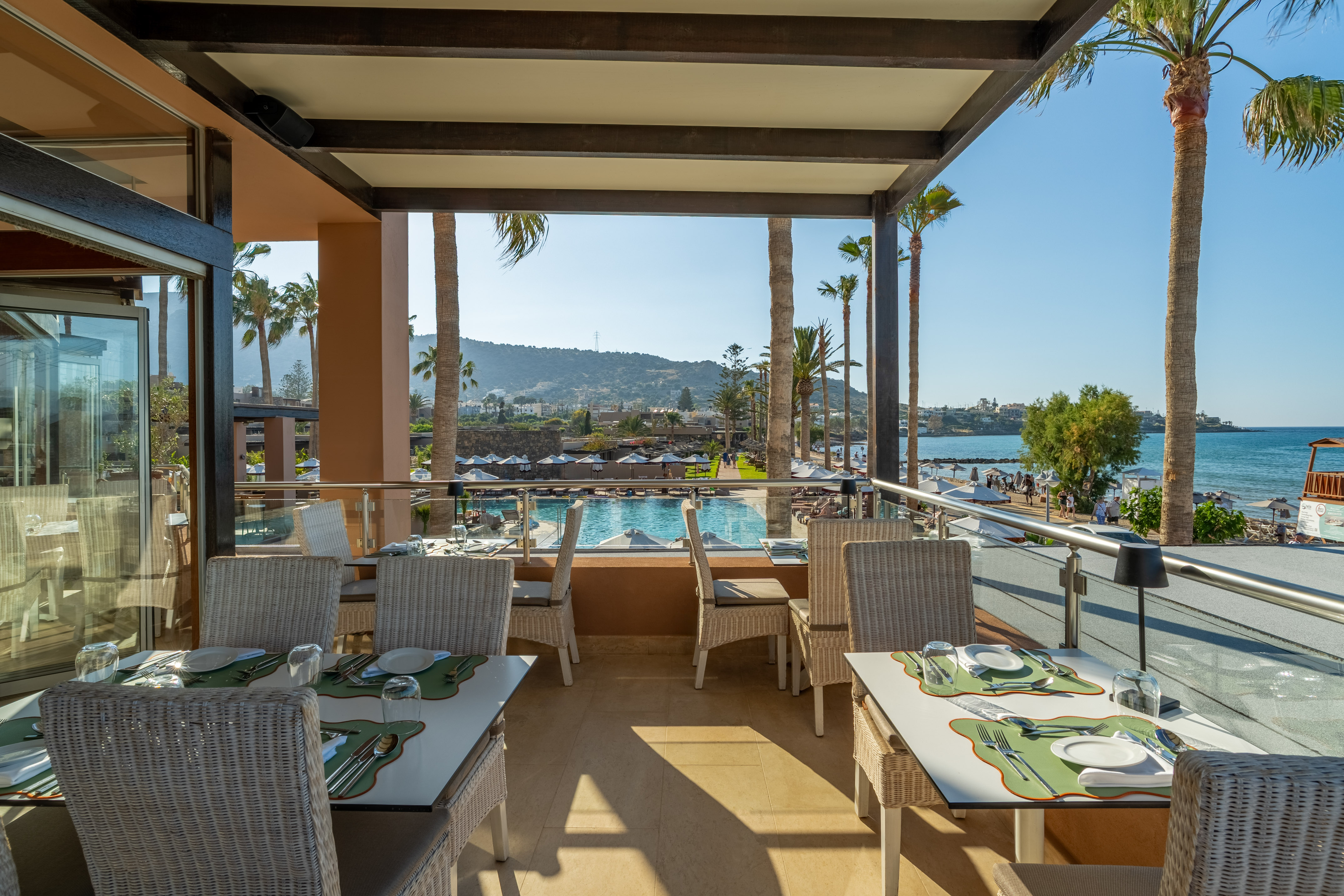 Beachfront restaurant terrace with pool, sea views, and palm trees.