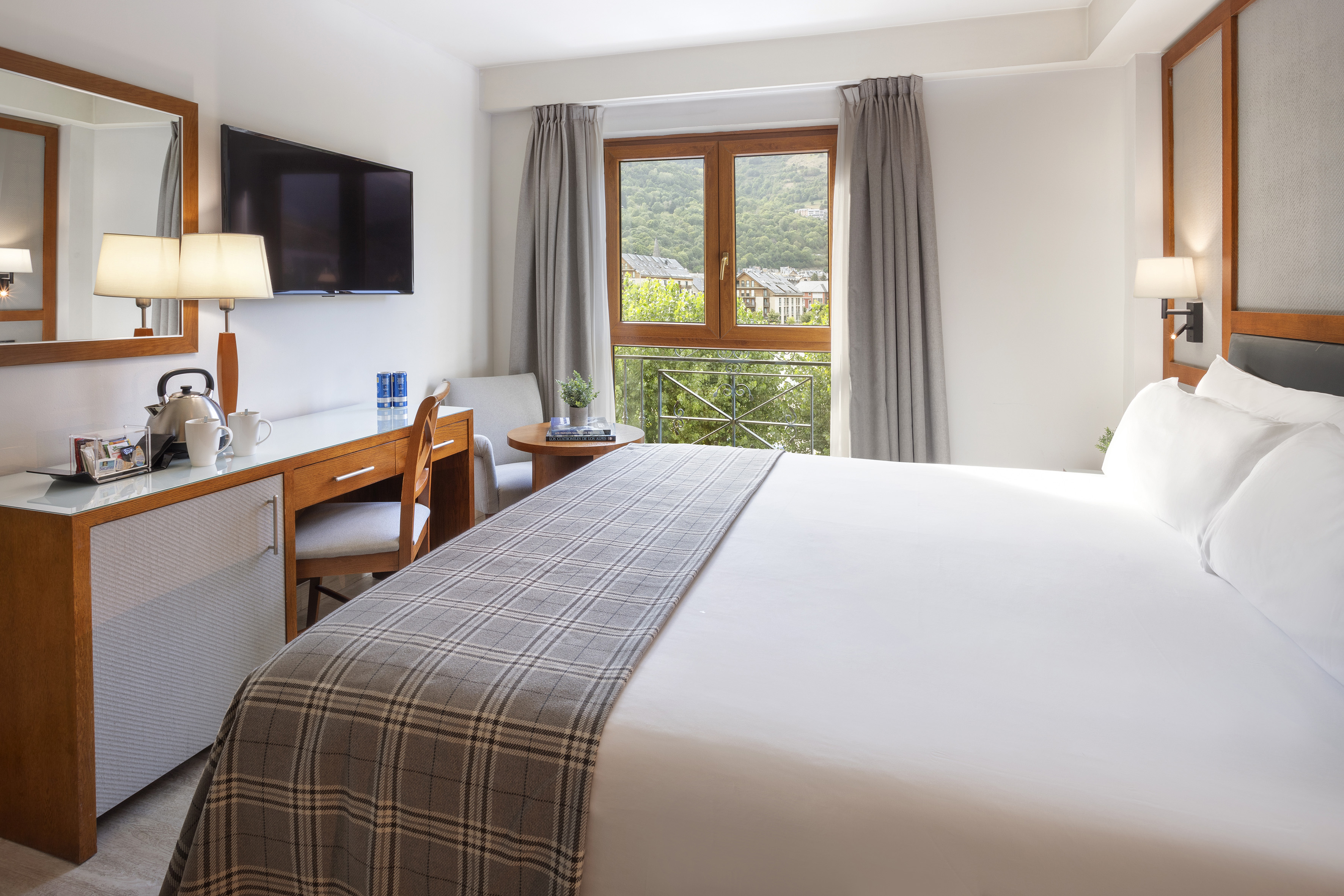 Cozy hotel room with bed, desk, flat-screen TV, and scenic mountain view.