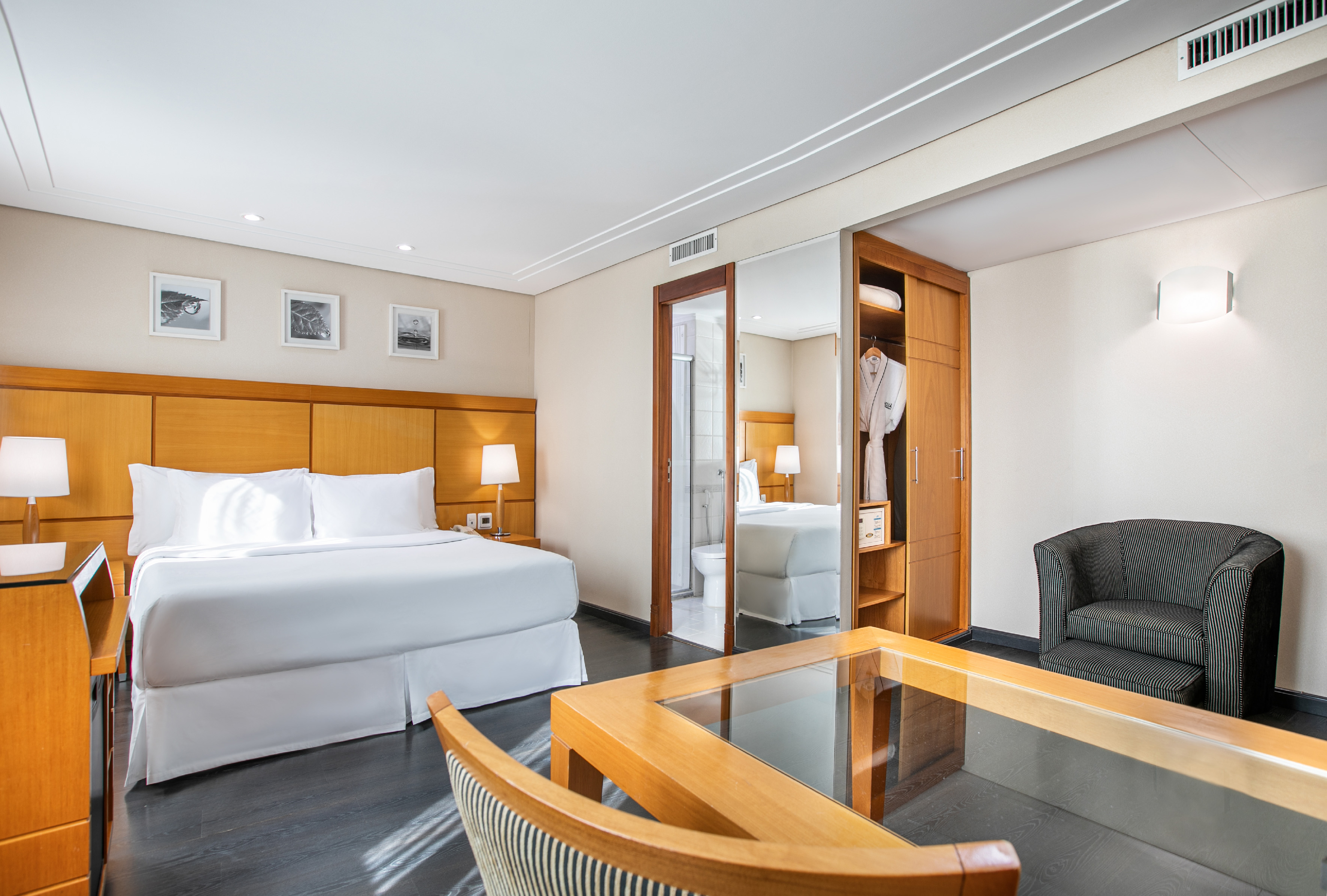 Modern hotel suite with large bed, desk, armchair, and visible bathroom.