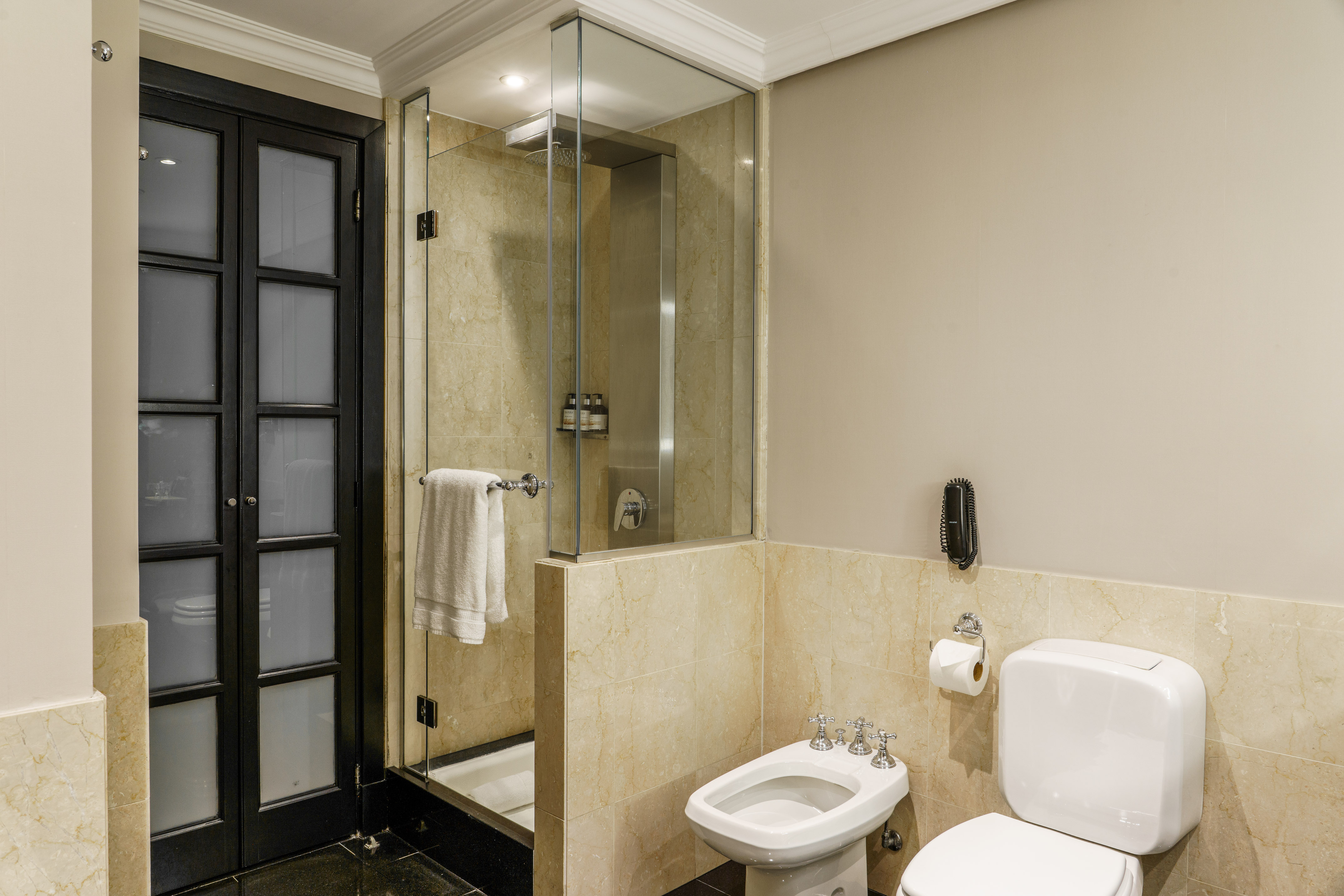 Modern hotel bathroom with marble tiles, glass shower, toilet, and bidet.
