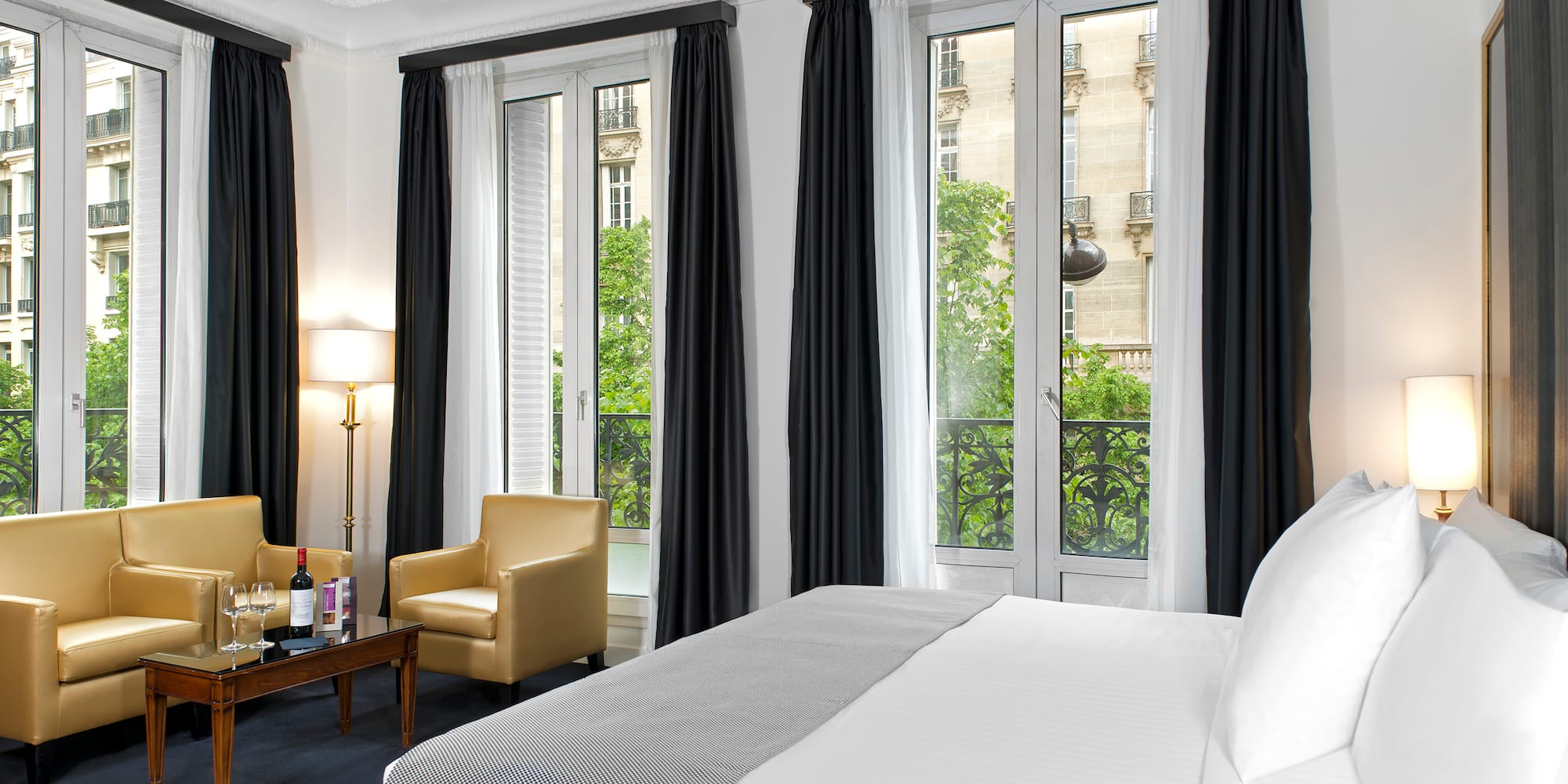 Elegant hotel suite with bed, yellow lounge seating, and city view windows.