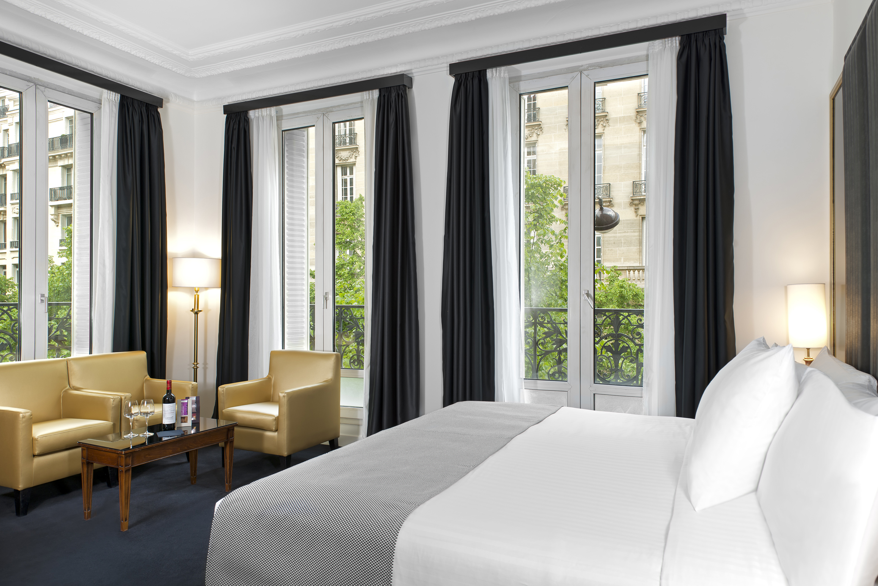 Elegant hotel suite with bed, yellow lounge seating, and city view windows.