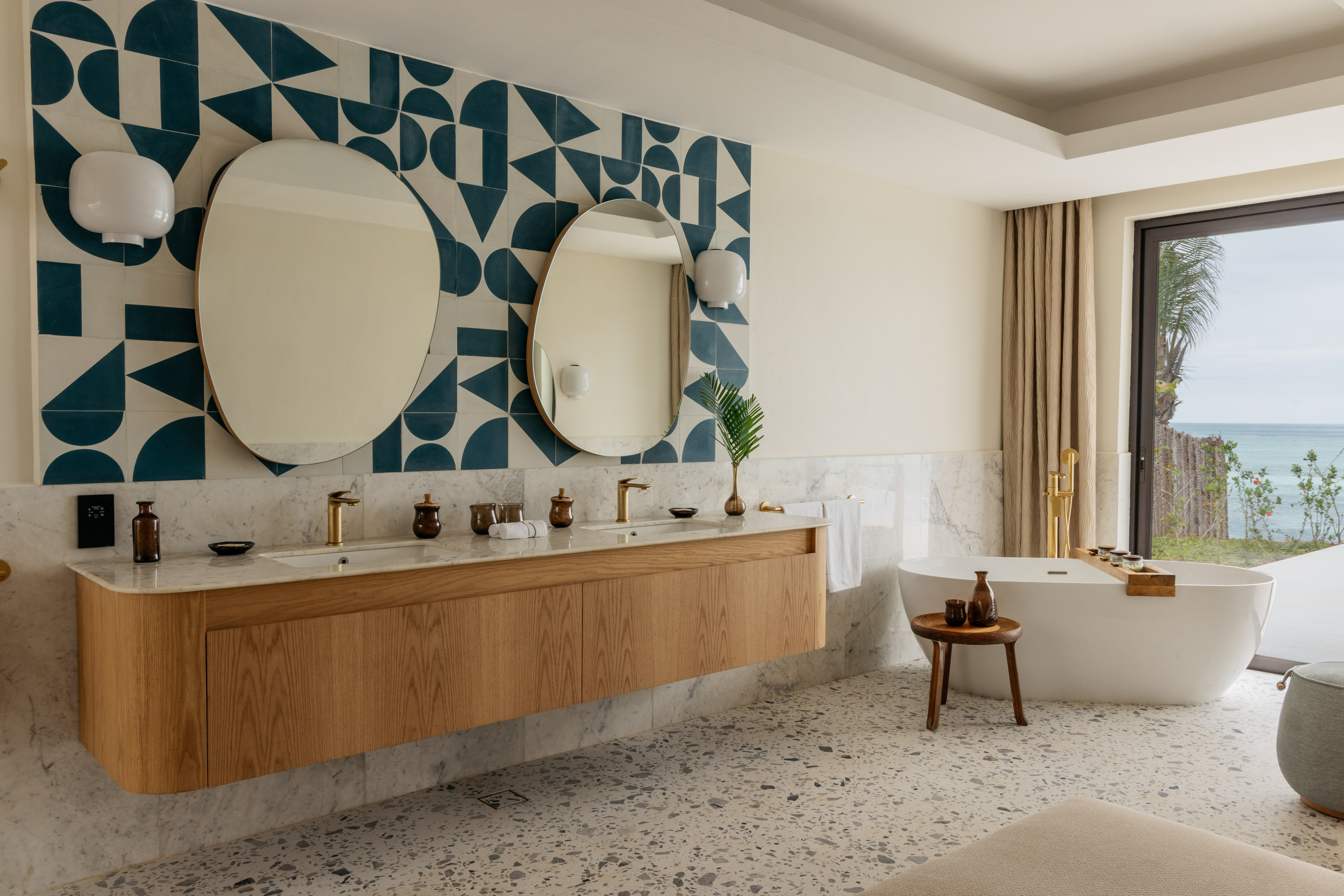 Elegant bathroom: double vanity, geometric tiles, freestanding tub, ocean view.
