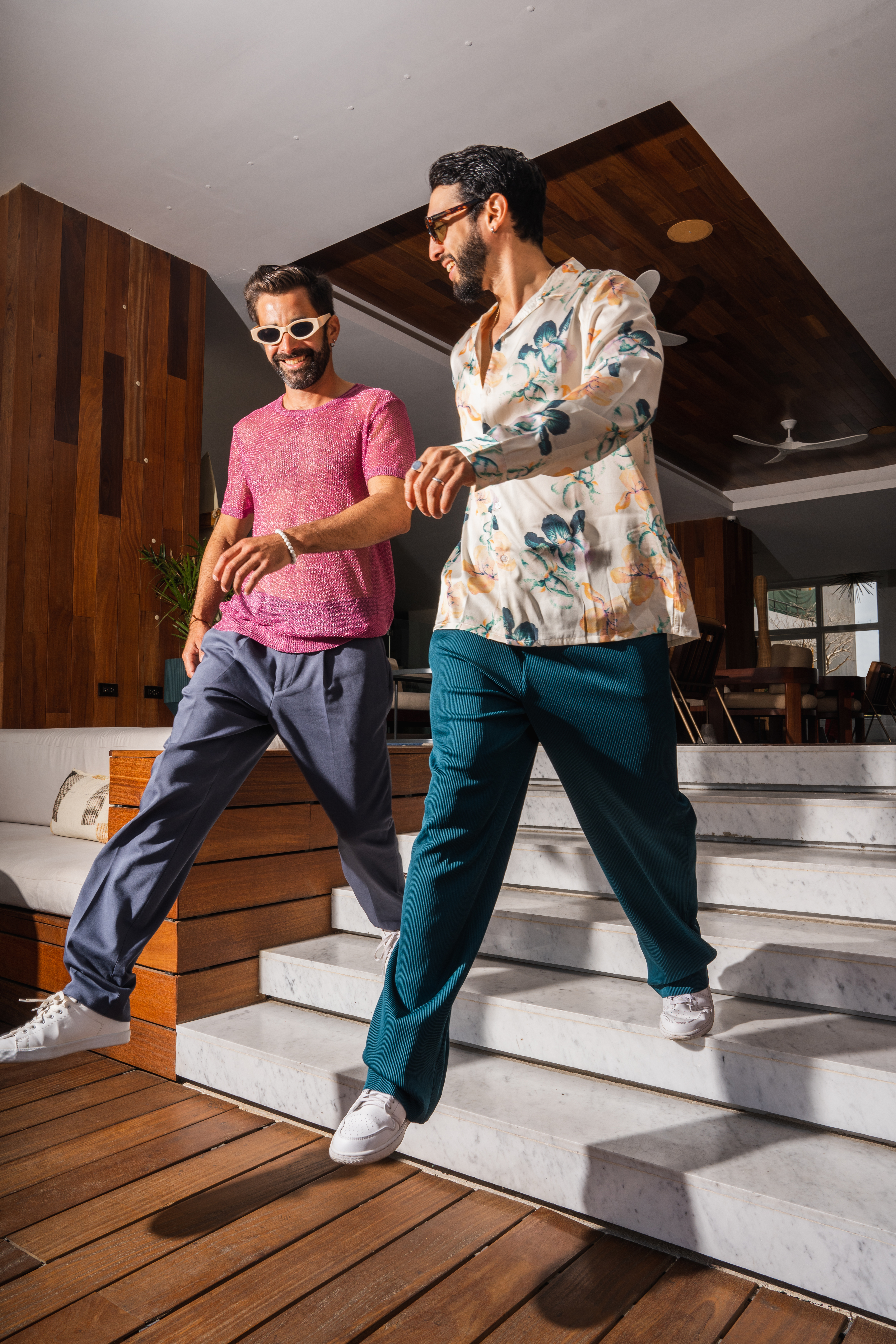 Two men in stylish summer fashion walking down modern marble stairs.