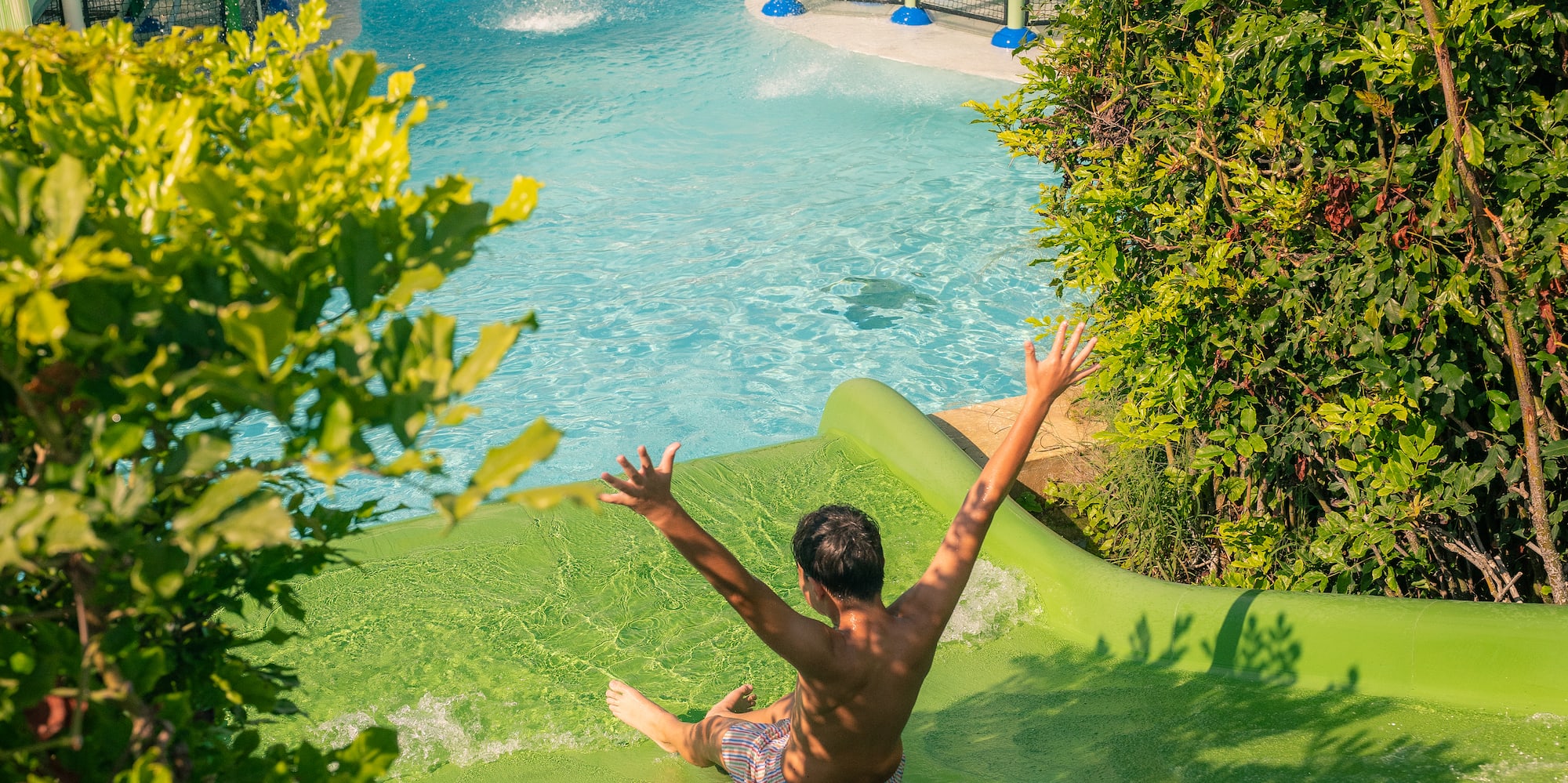 Boy sliding down green water slide at resort water park.