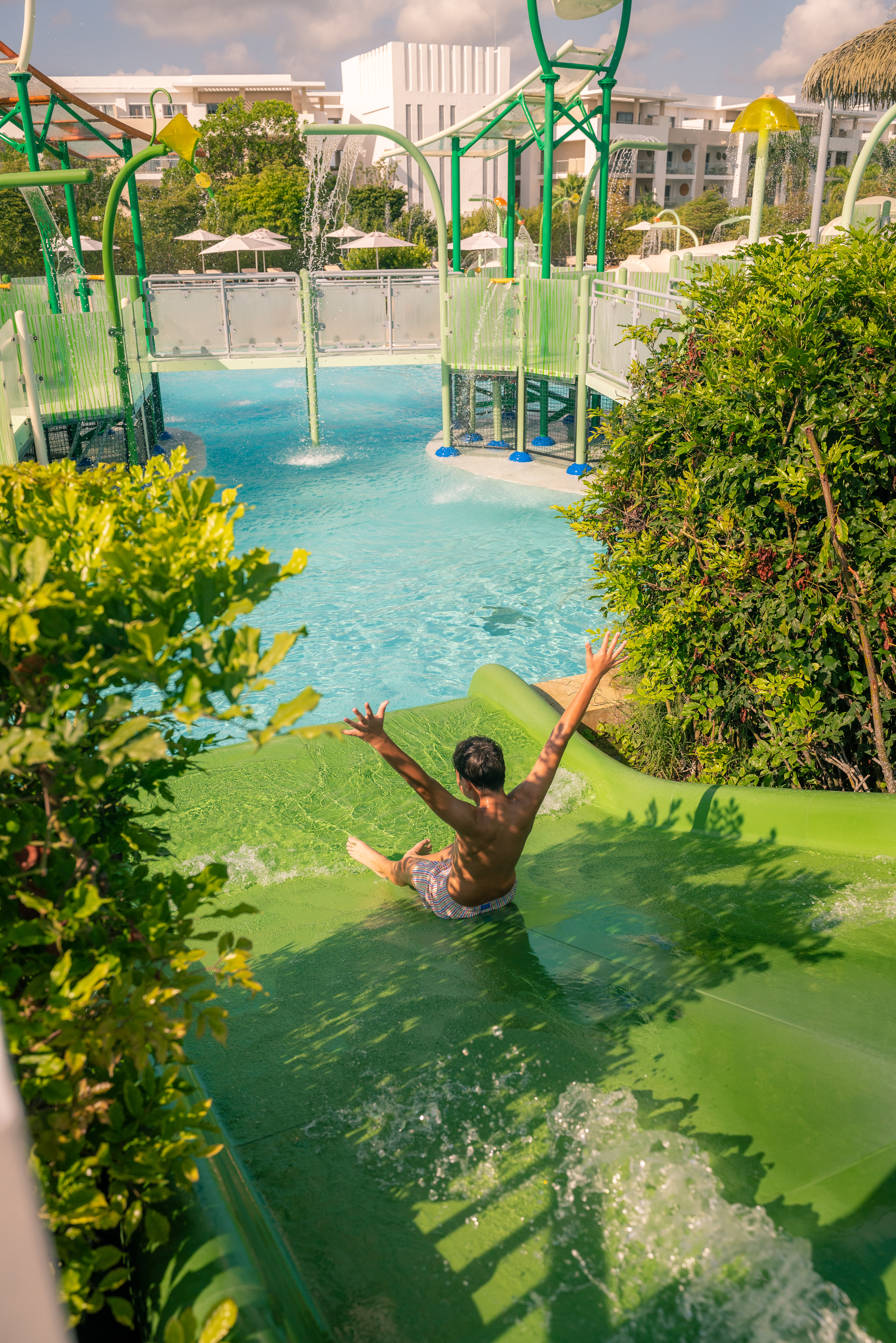 Boy sliding down green water slide at resort water park.