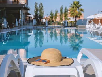 a hat and sunglasses on a white chair next to a pool