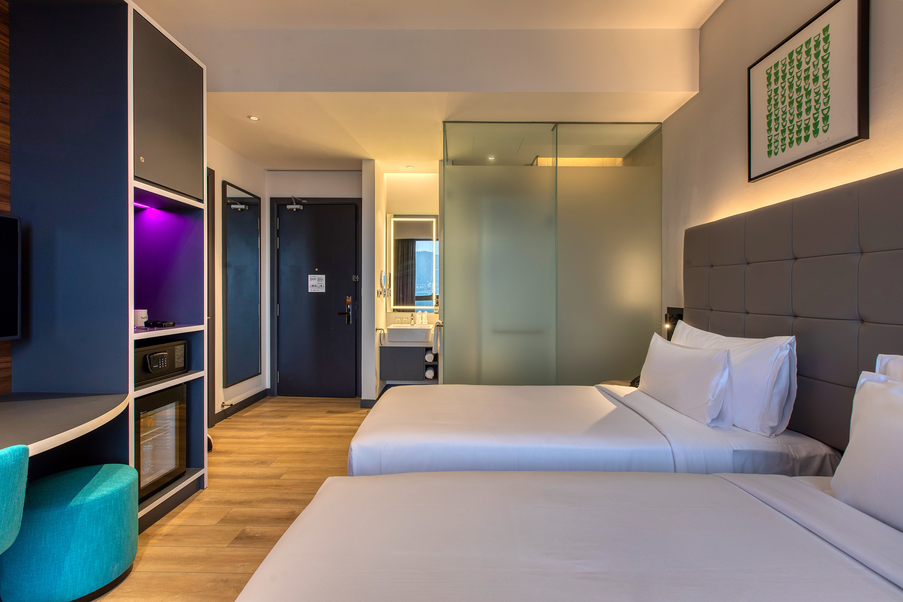 Modern hotel room with two twin beds, built-in desk, and glass bathroom.