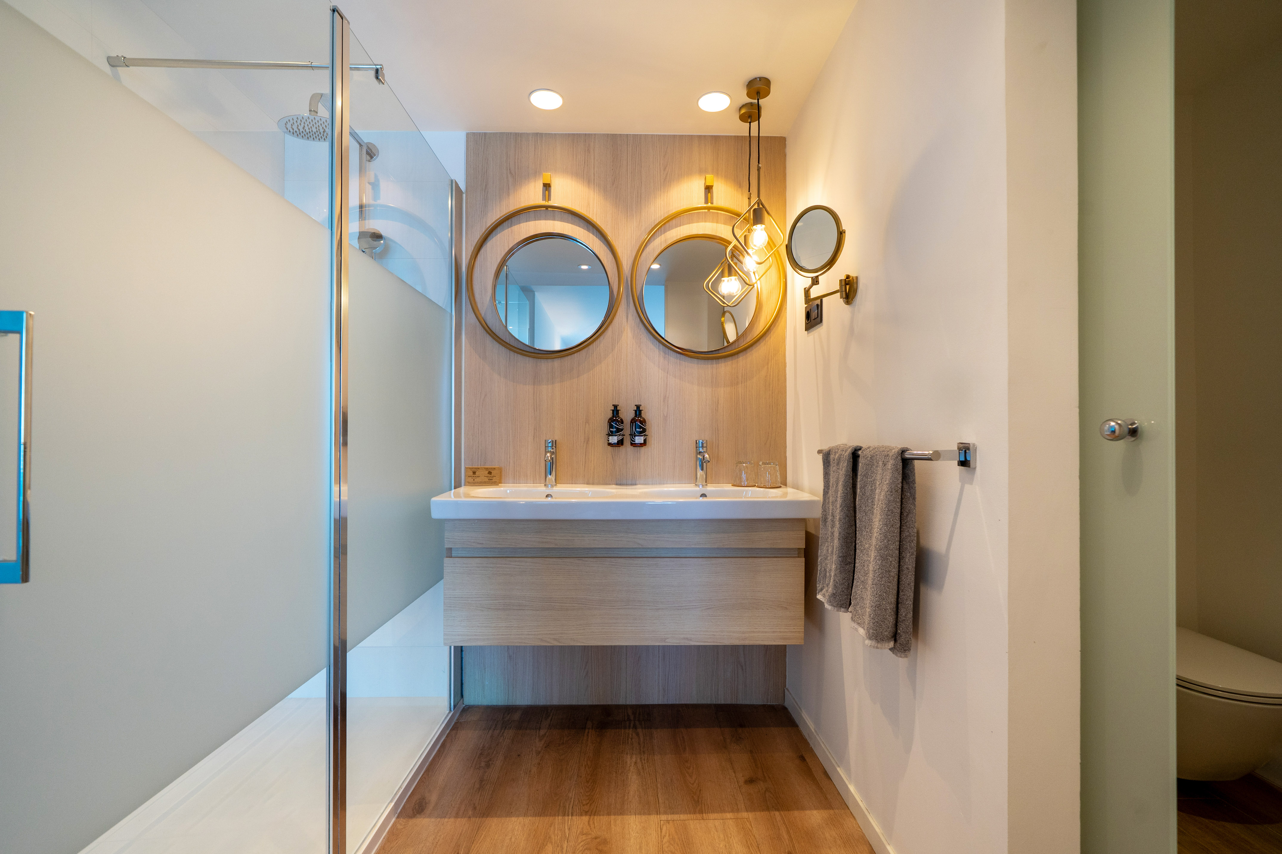 Modern hotel bathroom with double vanity, gold mirrors, and walk-in shower.