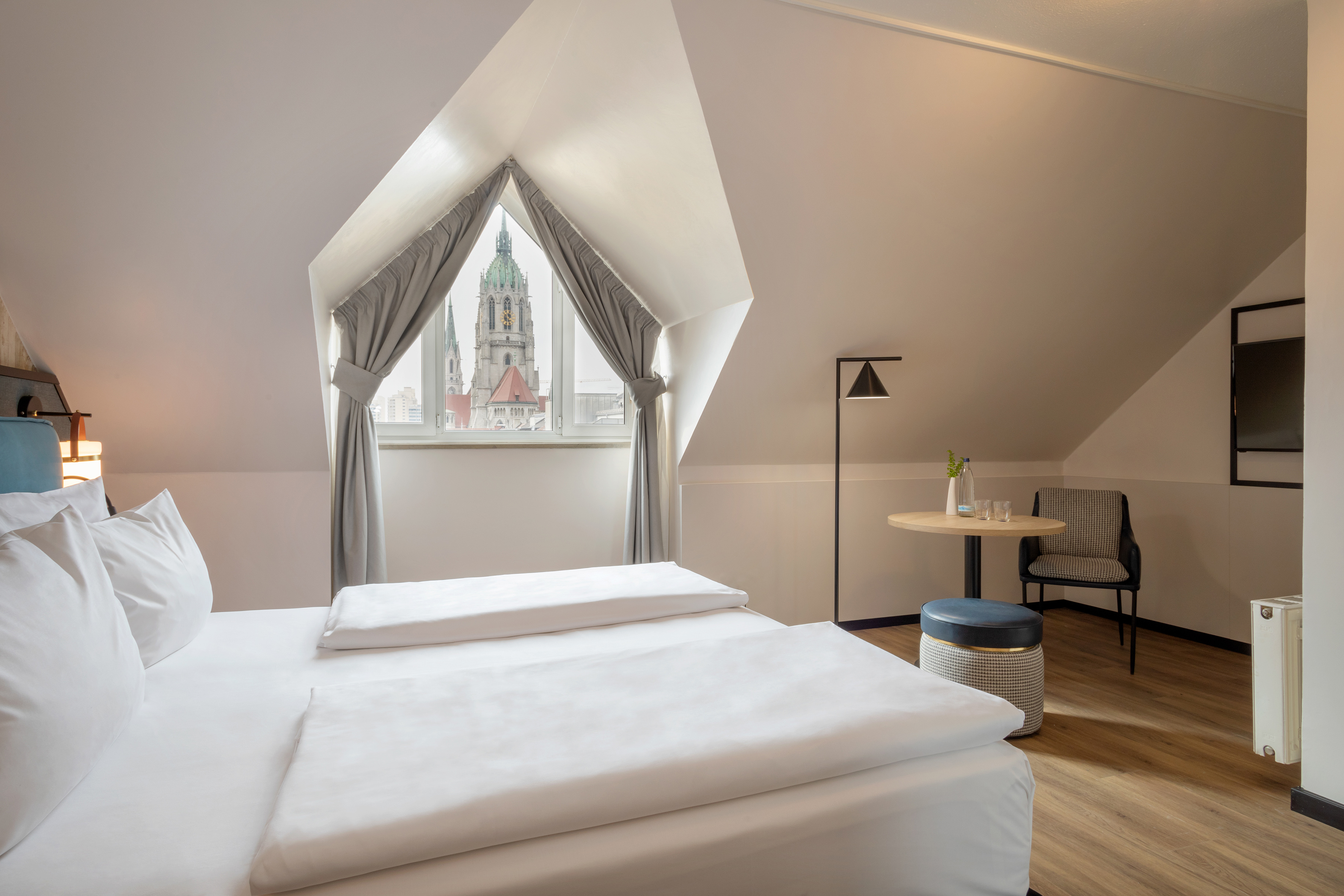 Hotel attic room with bed and window view of a historic city tower.