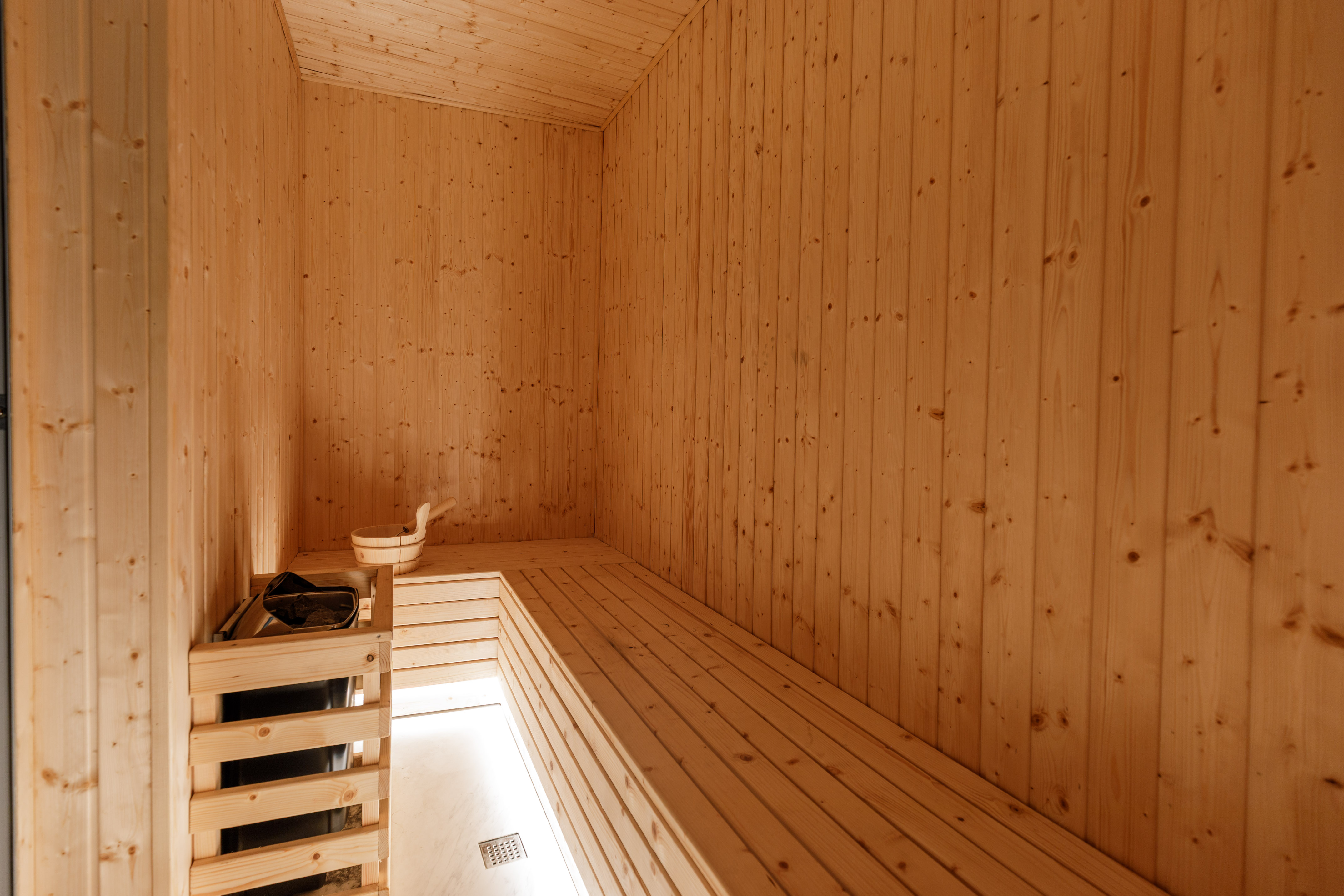 Sauna room interior with wooden benches, heater, and bucket.