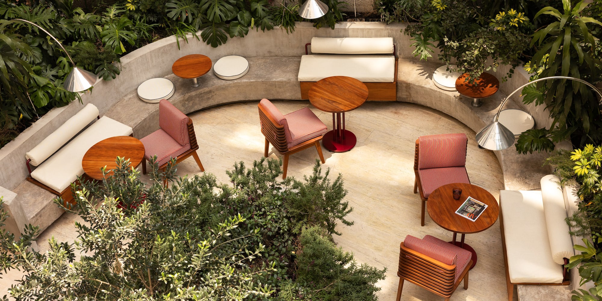 Modern outdoor patio lounge with concrete seating, wooden chairs, and lush greenery.