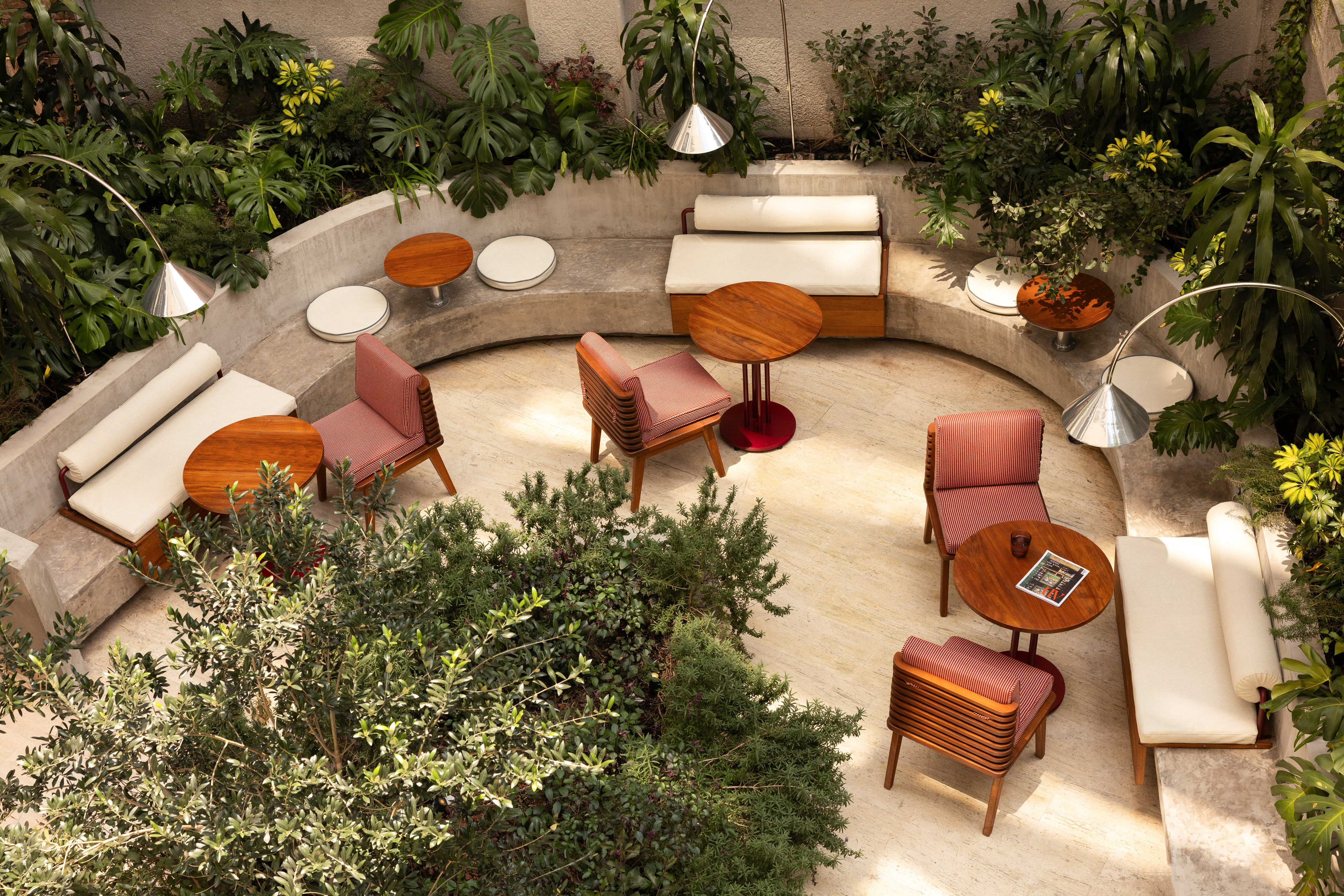 Modern outdoor patio lounge with concrete seating, wooden chairs, and lush greenery.