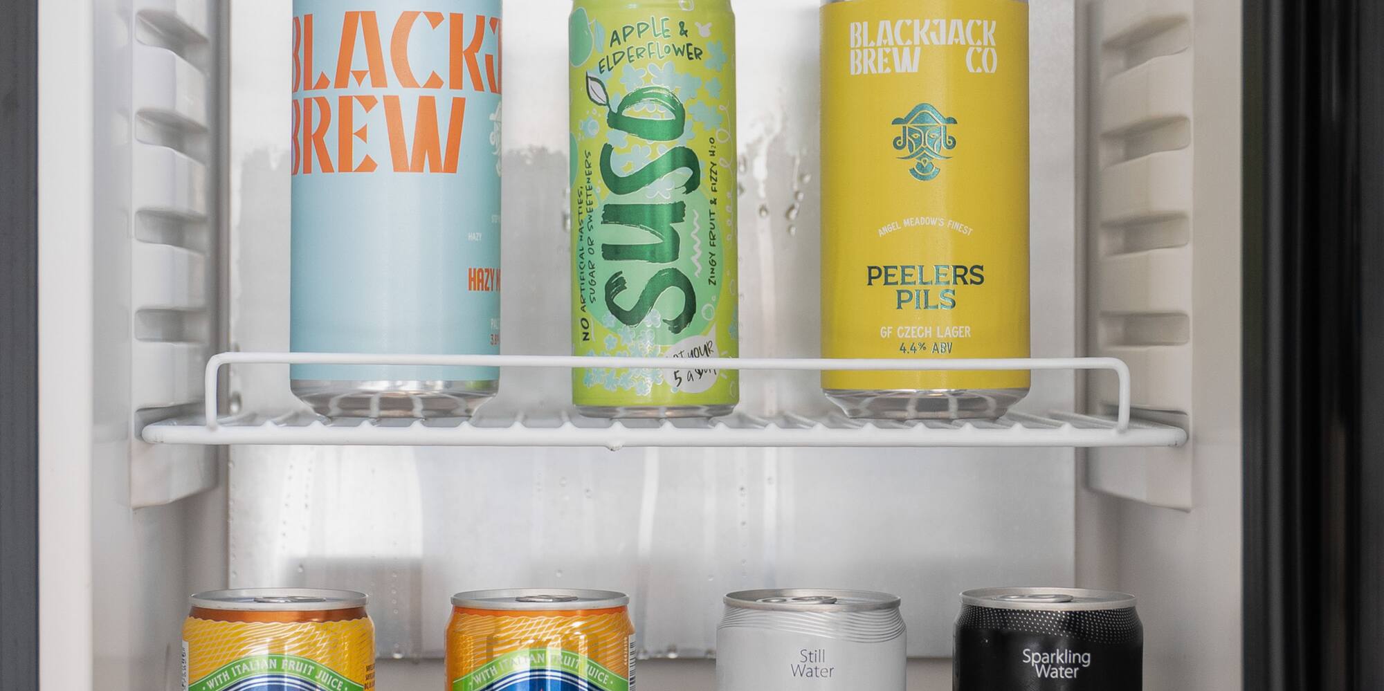 Mini fridge stocked with various canned beverages: beers, sparkling water, and sodas.