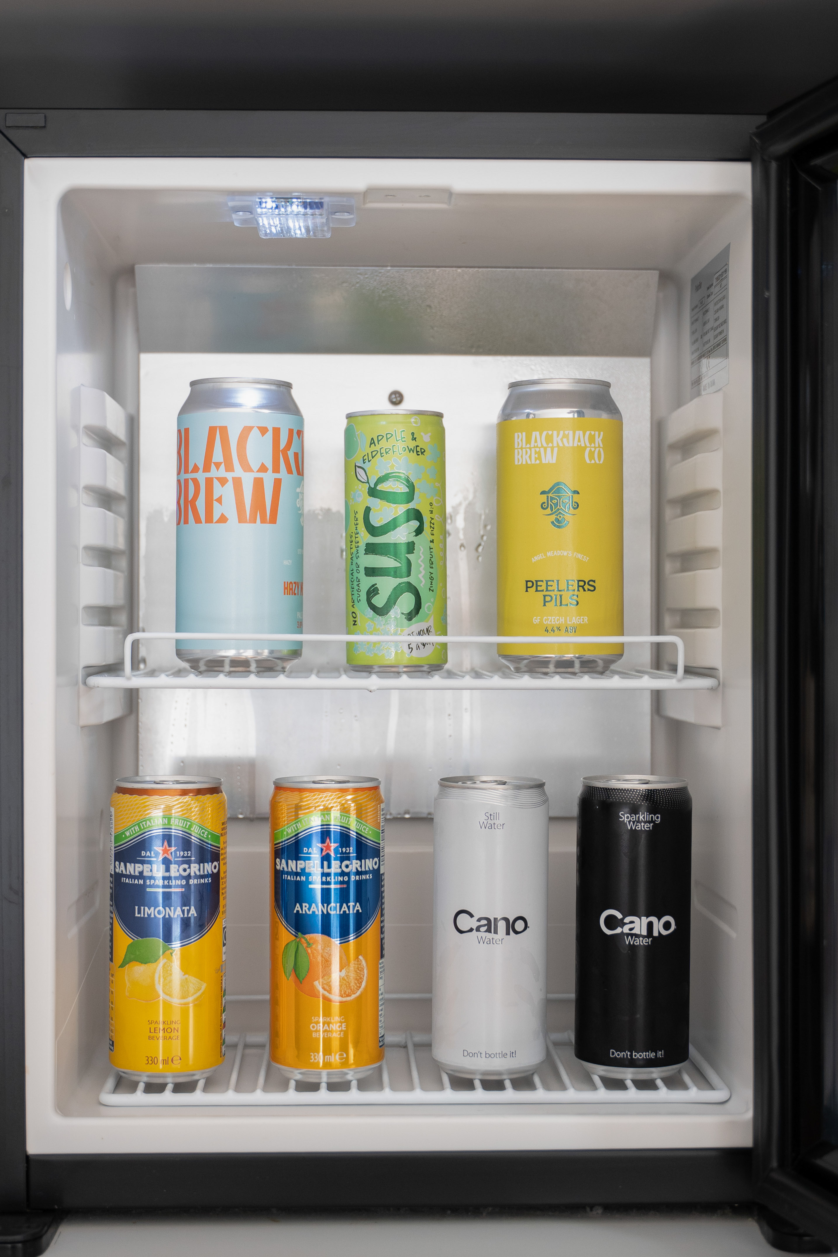 Mini fridge stocked with various canned beverages: beers, sparkling water, and sodas.