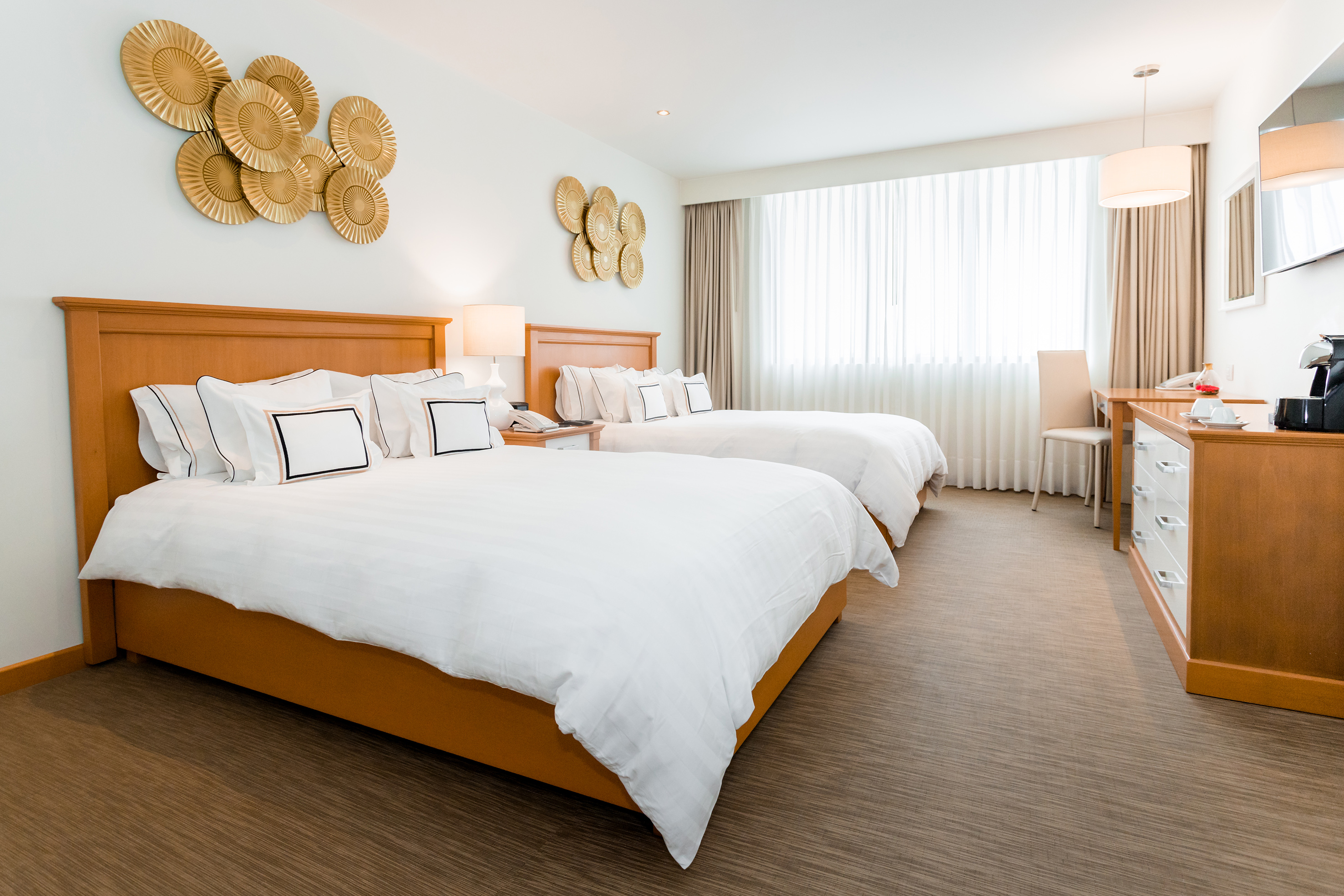 Modern hotel room with two twin beds, white bedding, and golden wall art.